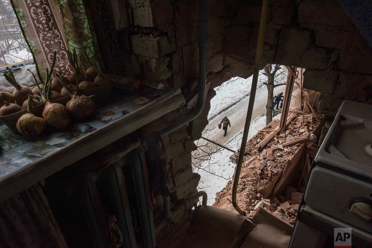  In this Saturday, Feb. 4, 2017 photo, a local resident walking in a street is seen through a hole in an apartment building damaged by shelling in Avdiivka, Ukraine. Fighting in eastern Ukraine sharply escalated this week. The Ukrainian command said 