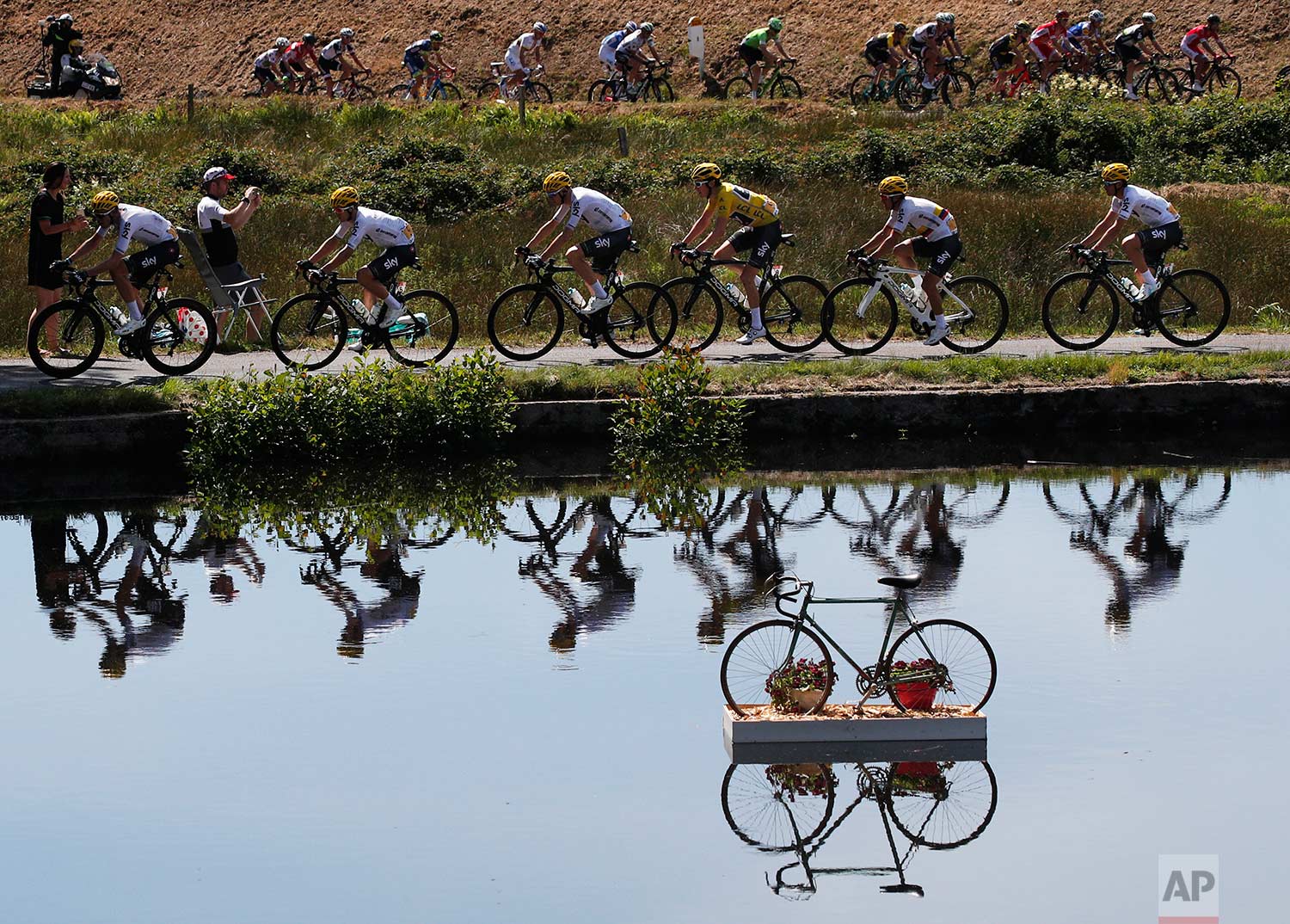  In this Wednesday, July 5, 2017 photo, Britain's Geraint Thomas, wearing the overall leader's yellow jersey, and new overall leader Britain's Chris Froome, left of Thomas, are reflected in a pond as they ride in the pack during the fifth stage of th