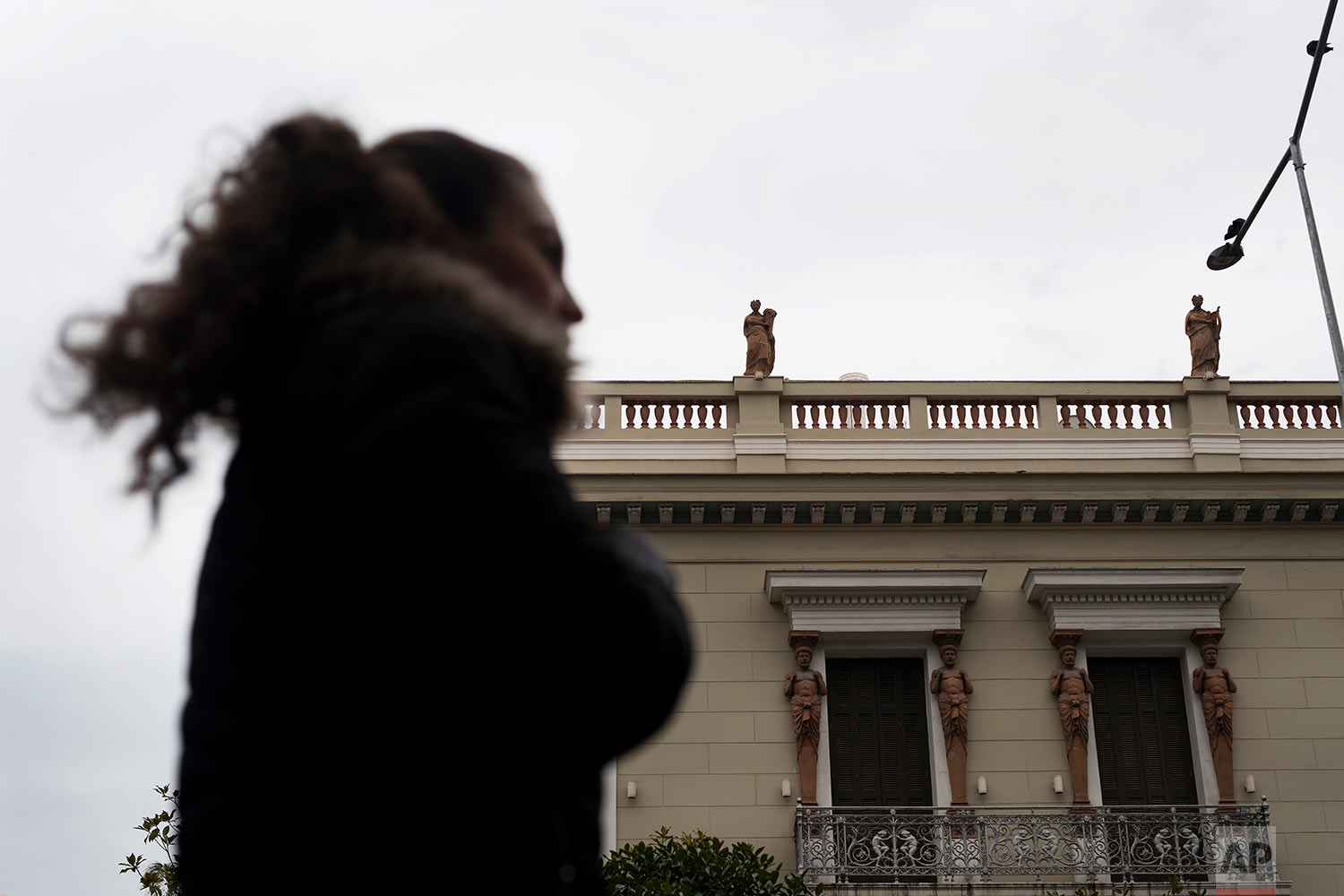  In this Thursday, Dec. 21, 2017 photo, a woman walks past a neoclassical building decorated with terracotta statues of the muses, on the roof, and Atlases, flanking the windows, made by sculptor and ceramicist Haralambos Goumas in Piraeus, the port 