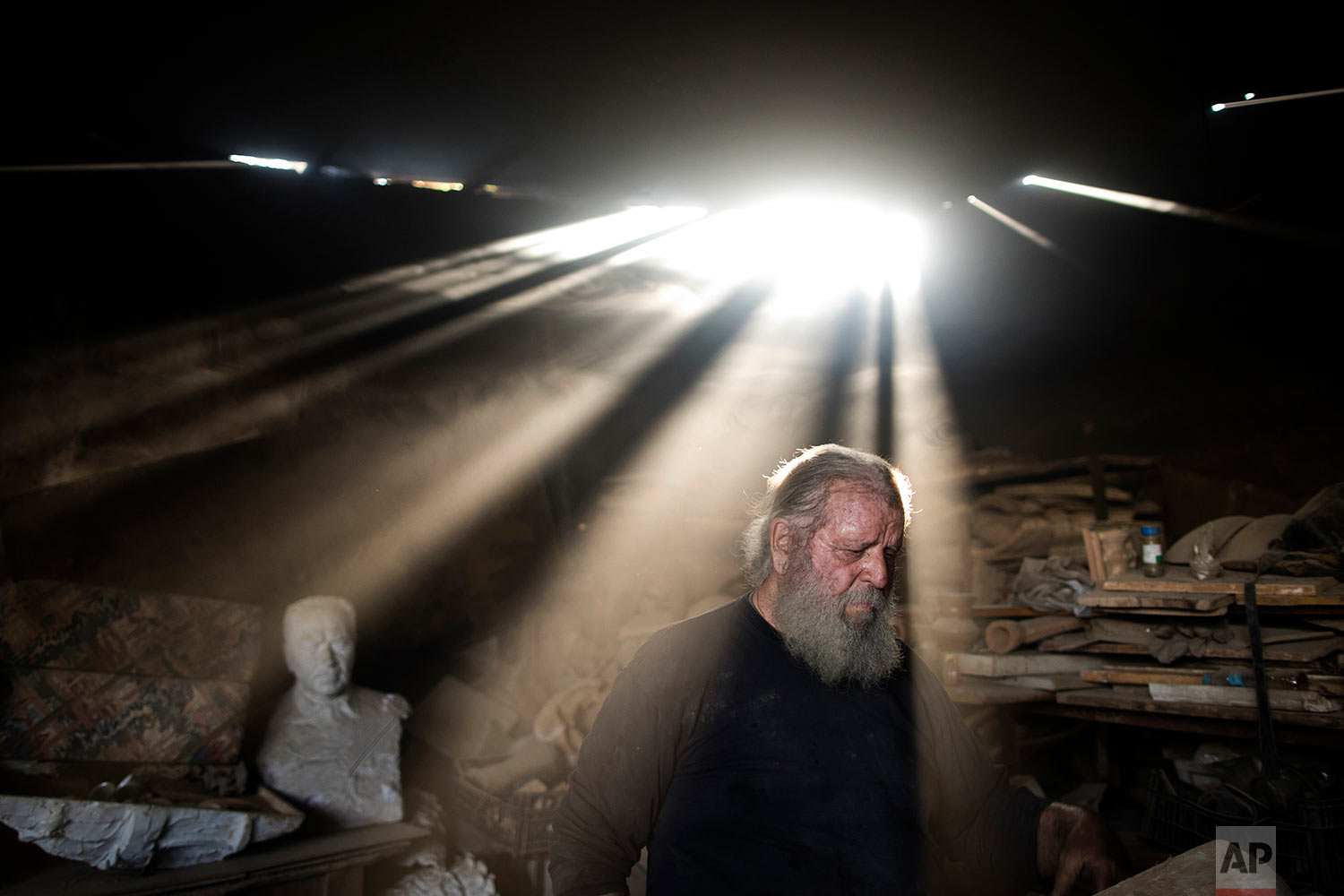  In this Friday, Nov. 20, 2017 photo, rays of sunlight shine on sculptor and ceramicist Haralambos Goumas as he works in his workshop, in the Egaleo suburb of Athens. (AP Photo/Petros Giannakouris) 