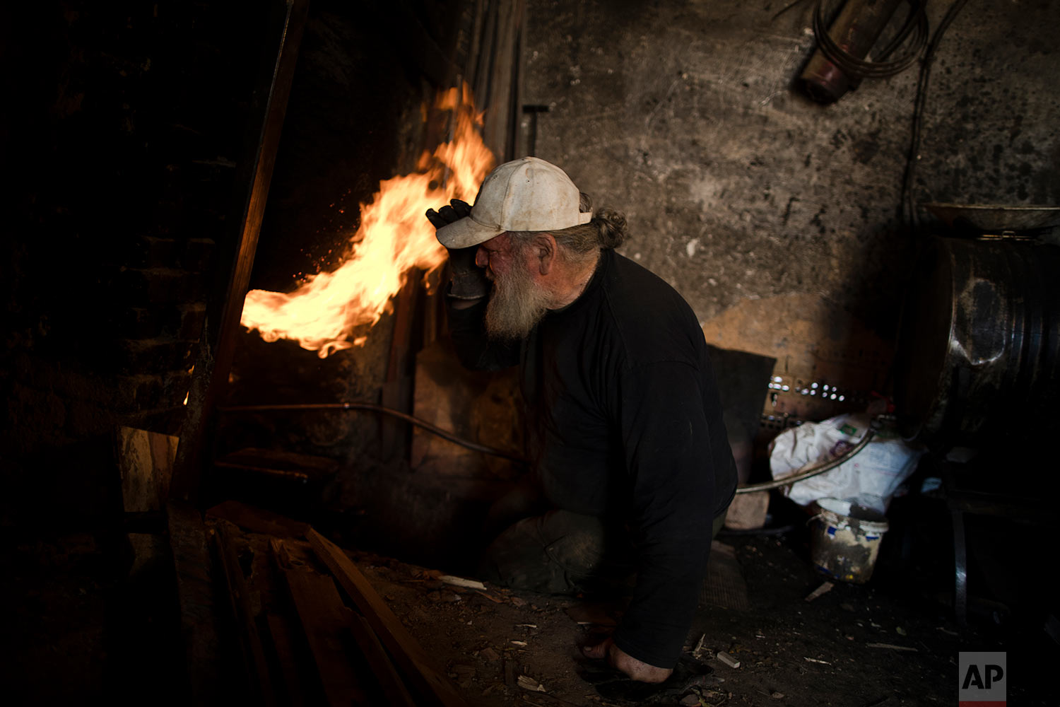  In this Friday, Nov. 20, 2017 photo, sculptor and ceramicist Haralambos Goumas looks into the fire as he tries to control the temperature of the furnace in his workshop in the Egaleo suburb of Athens. (AP Photo/Petros Giannakouris) 