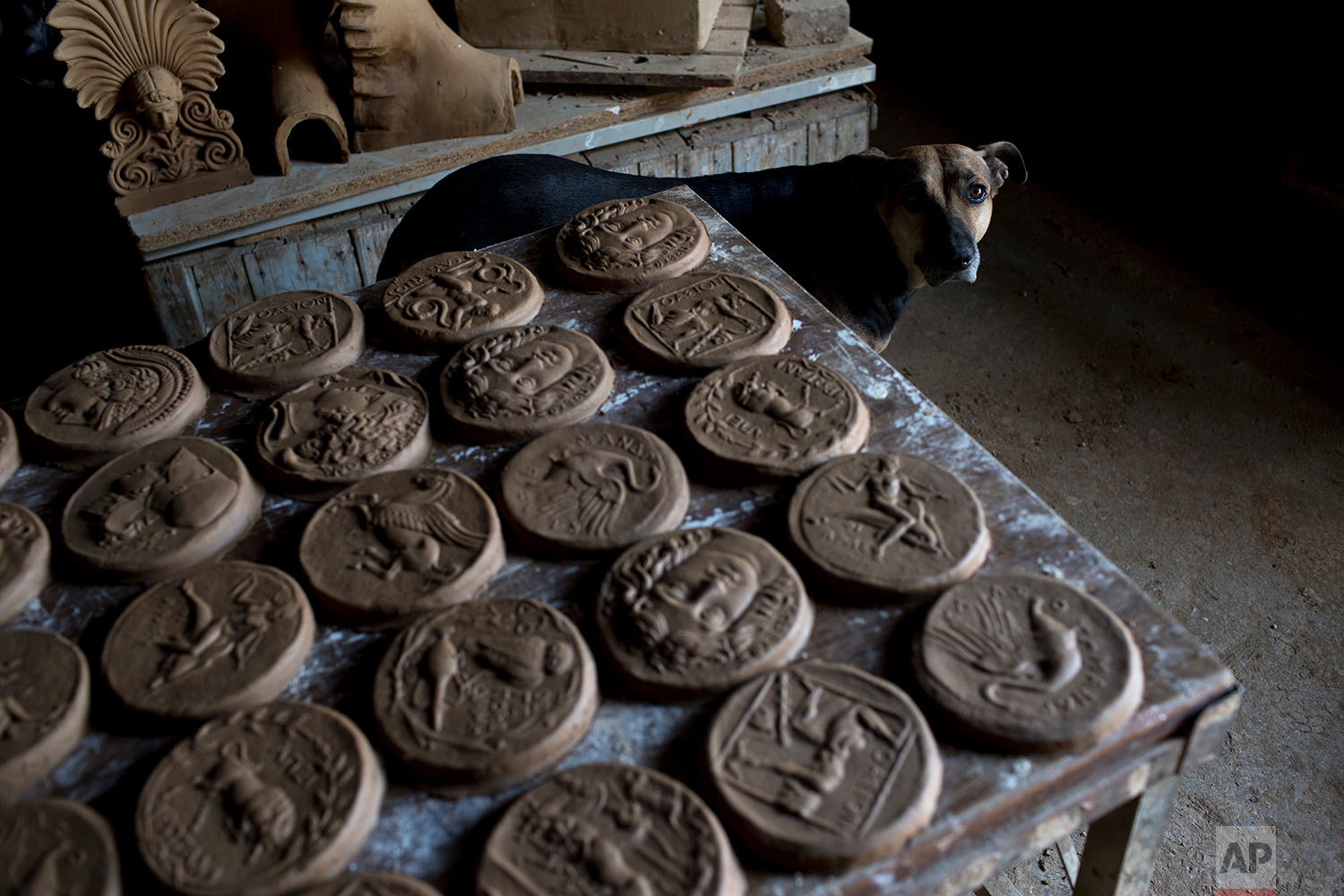  In this Friday, Oct. 13, 2017 photo a dog stands next to ceramic medallions based on ancient Greek coins in Haralambos Goumas' sculpture and ceramic workshop, in the Egaleo suburb of Athens. (AP Photo/Petros Giannakouris) 