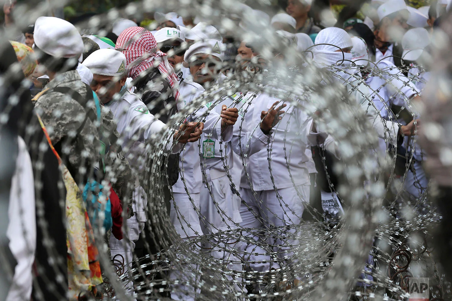 In this Wednesday, Sept. 6, 2017 photo, Muslim protesters are seen through razor wire barricades during a rally against the persecution of Rohingya Muslims outside the Myanmar's Embassy in Jakarta, Indonesia. Several thousand people marched in Indonesia's capital on Wednesday, calling on the government of the world's most populous Muslim nation to put more pressure on Myanmar to halt the persecution of its Rohingya Muslim minority. (AP Photo/Tatan Syuflana)