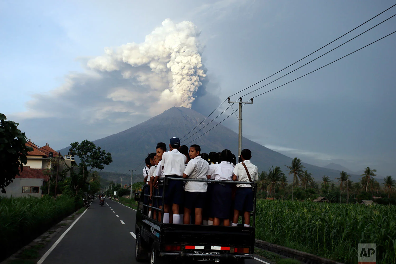 School students stand on a truck as their transport to go to school with the Mount Agung volcano spews smoke and ash in Karangasem, Bali, Indonesia, Tuesday, Nov. 28, 2017. Indonesia authorities raised the alert for the rumbling volcano to highest level on Monday and closed the international airport on the tourist island of Bali stranding some thousands of travelers.(AP Photo/Firdia Lisnawati)