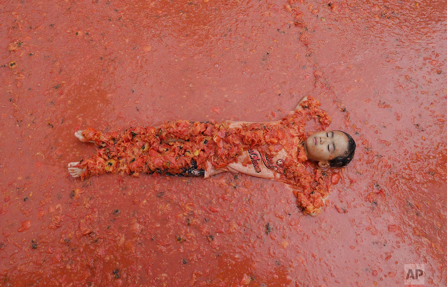 A boy lies in a pool of tomatoes during the 2017 Tomato Festival in Hwacheon, South Korea, Saturday, Aug. 5, 2017. The festival runs from Aug. 4 to Aug. 7. (AP Photo/Ahn Young-joon)