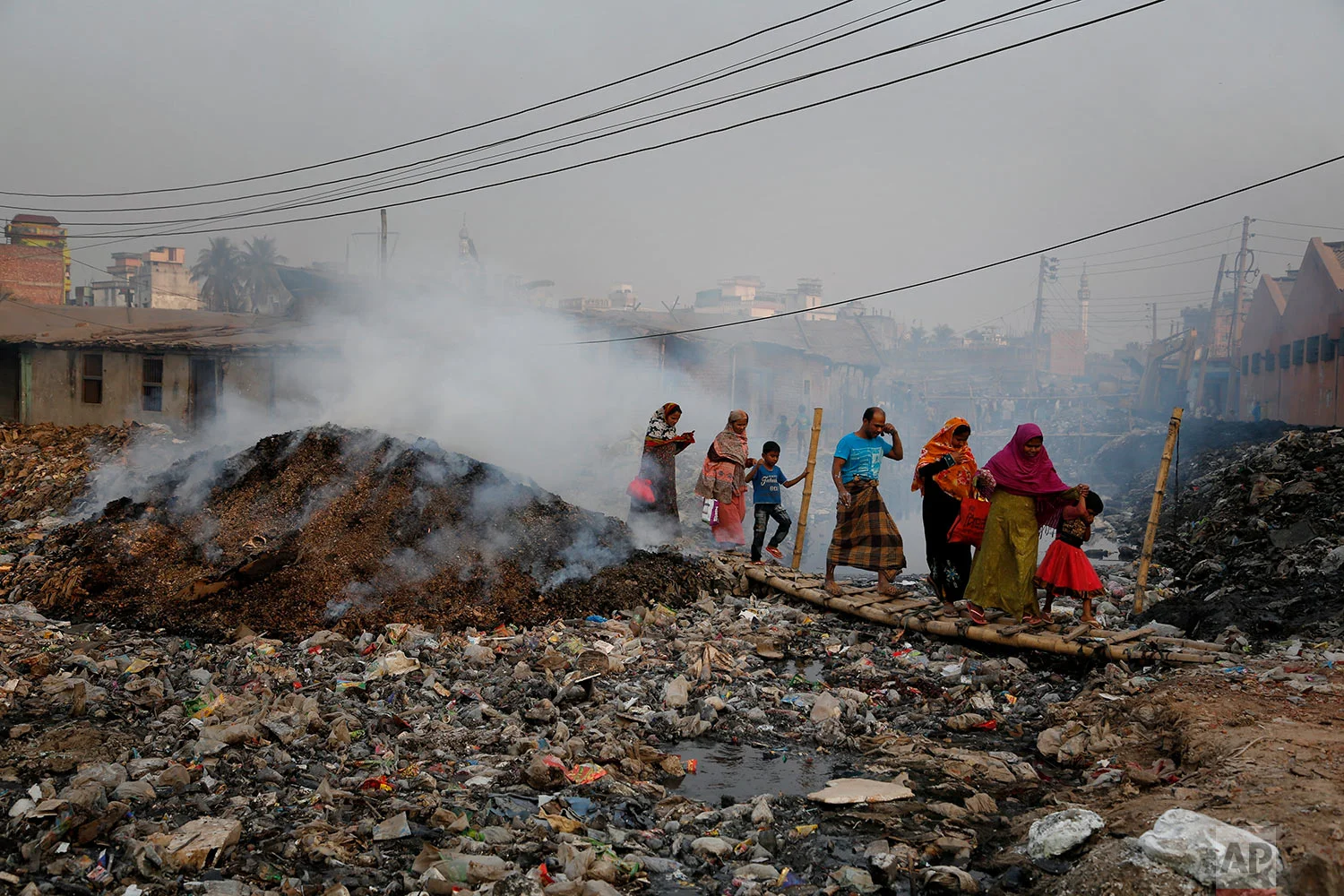 In this Monday, Feb. 6, 2017 photo, Bangladeshi people walk across a temporary bridge as smoke emits from tannery waste at the highly polluted Hazaribagh tannery area in Dhaka, Bangladesh. Pure Earth a nongovernmental organization that addresses industrial pollution put Hazaribagh on its Top 10 list of polluted places, along with Chernobyl, although similar problems of pollution and dangerous working conditions exist at tannery clusters in the Philippines and India as well. (AP Photo/A.M. Ahad, File)