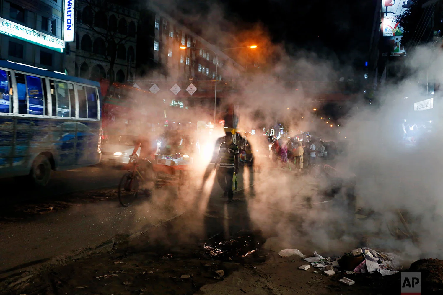 In this Wednesday, April 26, 2017 photo, a Bangladeshi man is silhouetted against the headlight of a car as he walks past smoke rising from a manhole on a hot summer evening in Dhaka, Bangladesh. (AP Photo/ A. M. Ahad)