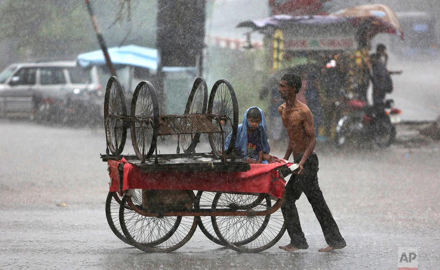An Indian man tries to protect his child from the pelting rain by covering him with his shirt as he pushes a handcart in Jammu, India, Wednesday, July 12, 2017. The monsoon season in India lasts from June to September is very crucial for India's agriculture sector that accounts for more than 13 percent of the economy and provides work for about half of the country's 1.25 billion people. (AP Photo/Channi Anand)