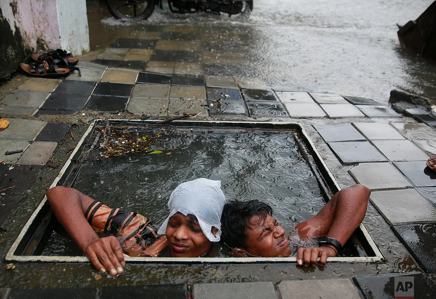 Municipal workers try to retrieve the lid of a manhole to prevent pedestrians from falling in, in Mumbai, India, Wednesday, Sept. 20, 2017. Incessant rainfall in India's commercial capital has affected air and rail traffic, and schools and colleges remained shut for the day. (AP Photo/Rafiq Maqbool)