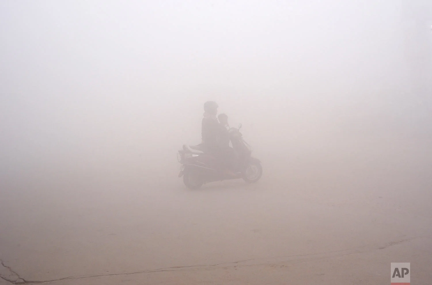 In this Thursday, Nov. 9, 2017, photo, a woman drives a scooter through the morning fog to drop off a child at school in Greater Noida, near New Delhi, India. A thick gray haze has enveloped India's capital region as air pollution hit hazardous levels. As winter approaches, a thick, soupy smog routinely envelops most parts of northern India, caused by dust, the burning of crops, emissions from factories and the burning of coal and piles of garbage as the poor try to keep warm. (AP Photo/R S Iyer)