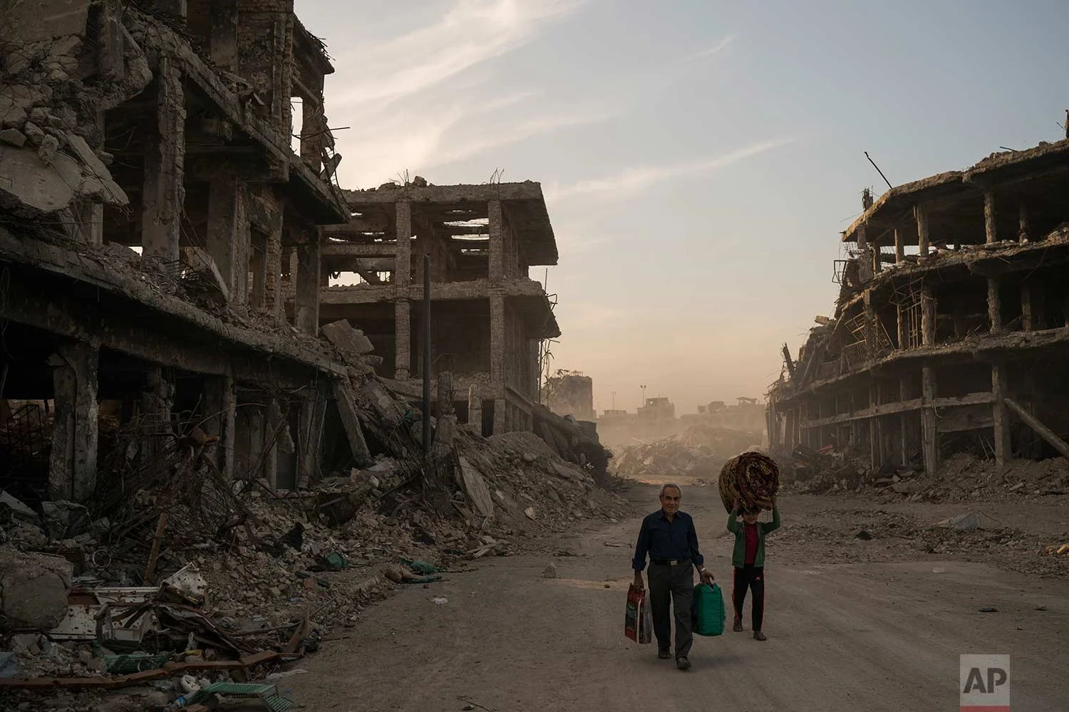 In this Nov. 15, 2017 photo, Haider, left, and Abdullah carry belongings they collected from their damaged house to wash before returning to live in the Old City of Mosul, Iraq. (AP Photo/Felipe Dana)