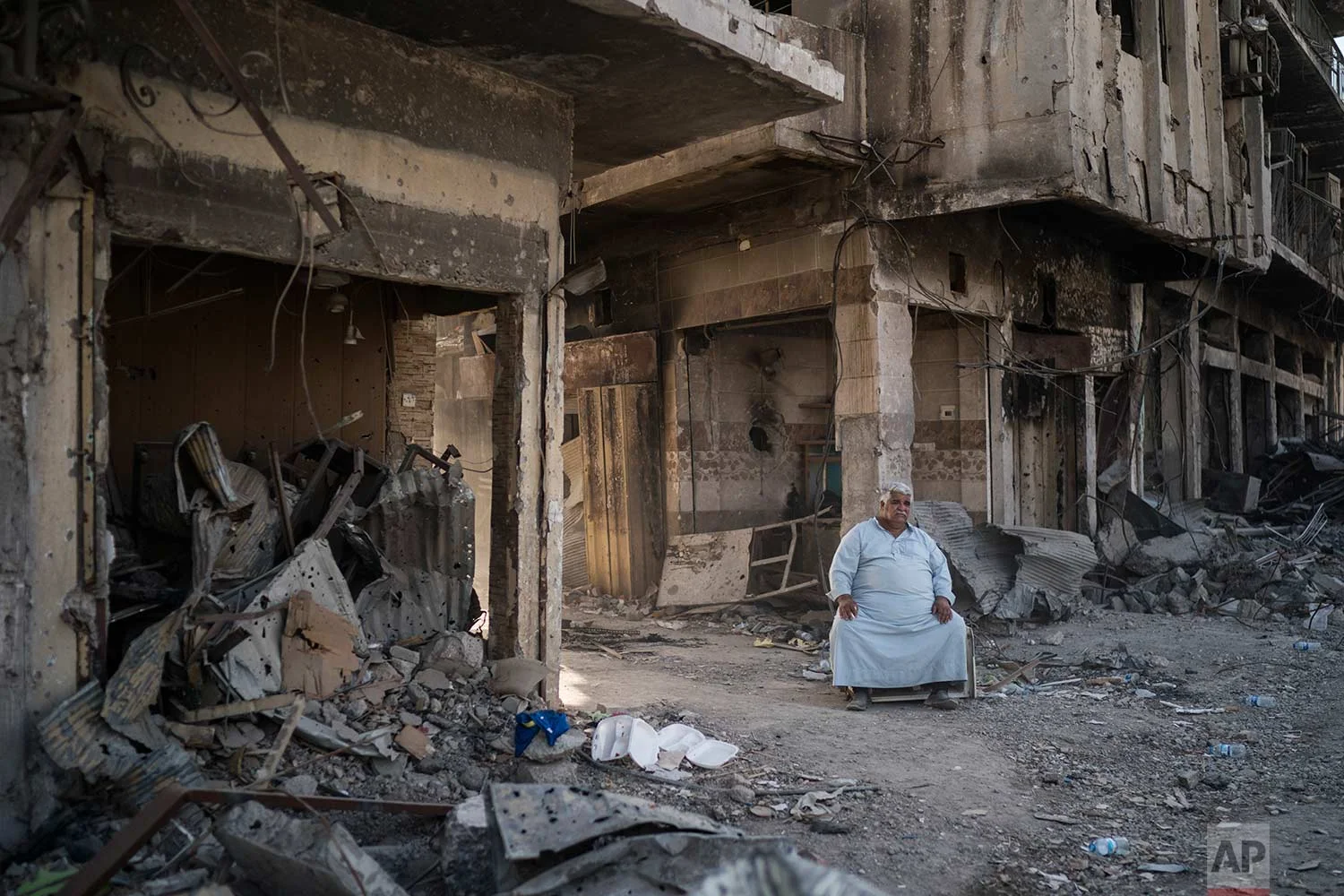 In this Nov. 18, 2017 photo, shop owner Abu Azar sits outside a destroyed bazaar in the Old City of Mosul, Iraq. (AP Photo/Felipe Dana)