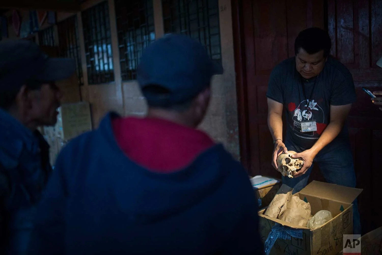 In this Nov. 29, 2017 photo, forensic anthropologist Dany Guzman holds a skull exhumed from a mass grave where residents hope to identify missing relatives among the unearthed bones of civil war victims, at a school in Santa Avelina, Guatemala. Guzman says that the vast majority of the bodies exhumed in Santa Avelina presented no sign of violent injuries, indicating that the victims perished from illness, malnutrition and other causes. (AP Photo/Luis Soto)