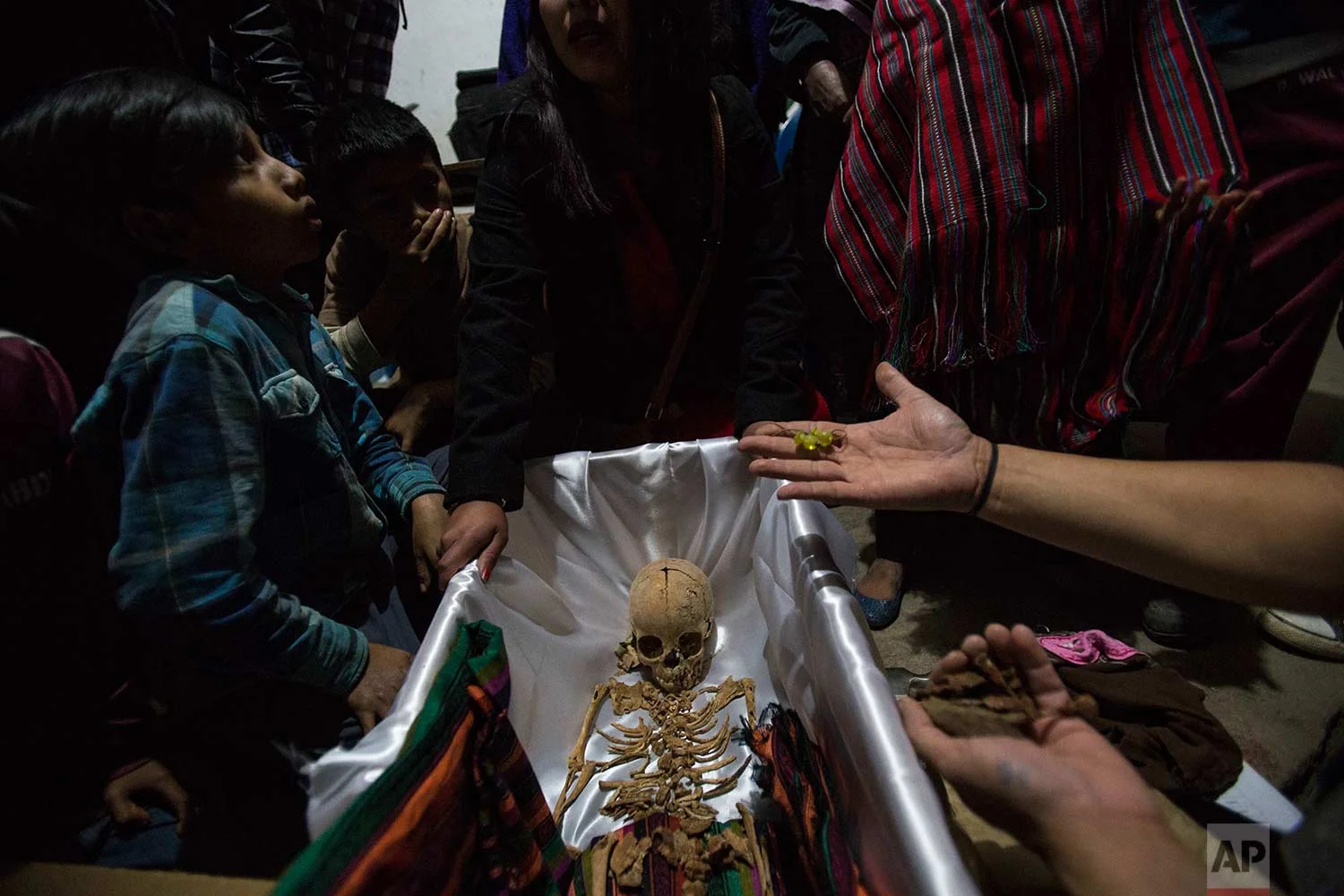 In this Nov. 29, 2017 photo, a forensic anthropologist holds earrings that belonged to 6-year-old Maria Poma Perez, who was exhumed from a mass grave, during her wake in Santa Avelina, Guatemala. The remains of Maria were recognized by her mother when she saw the clothes and earrings, one day before the mass burial of 172 civil war victims, including Maria. (AP Photo/Luis Soto)