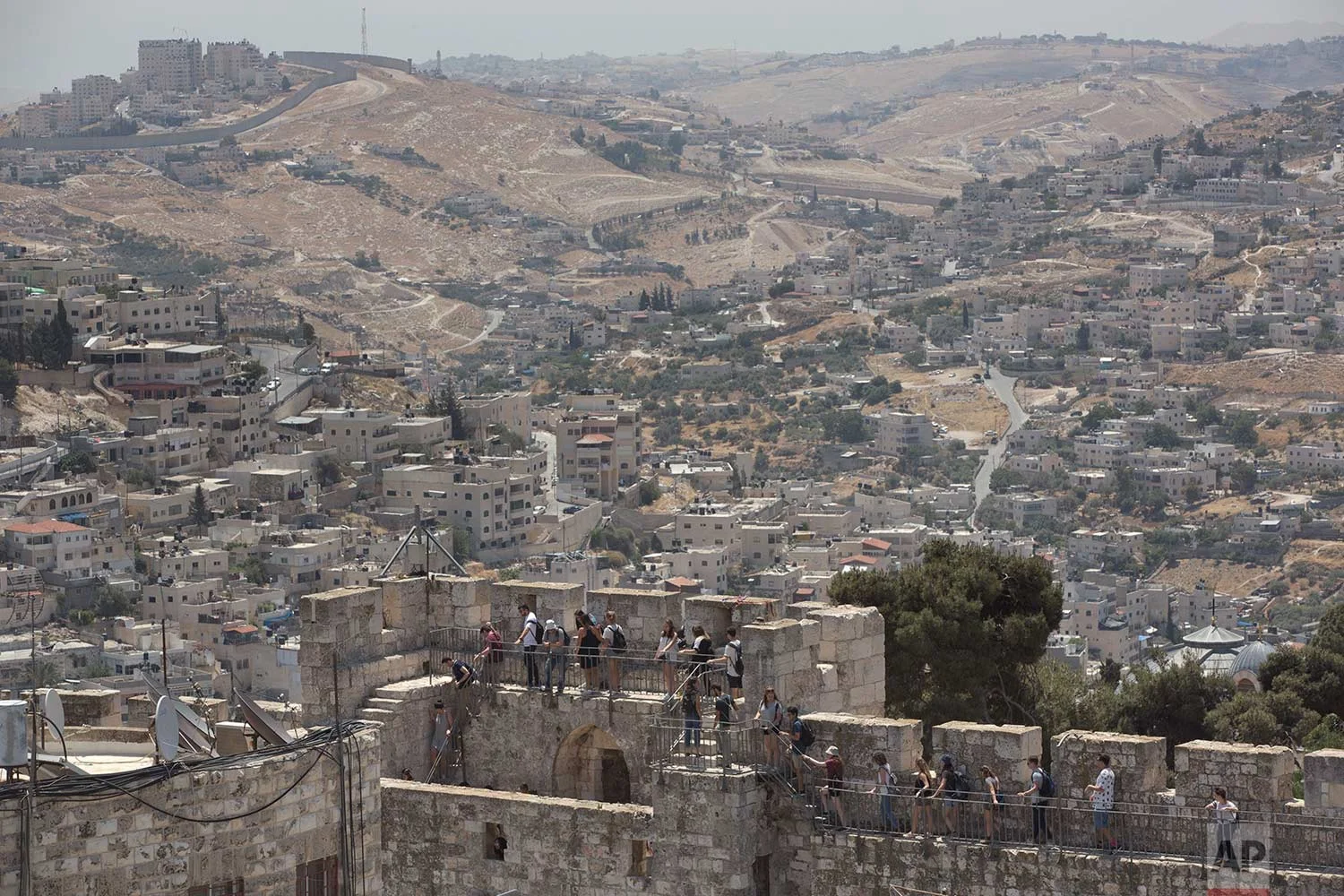 In this Wednesday, May 24, 2017 photo, backdropped by the Silwan neighborhood of east Jerusalem, people tour the Jerusalem Ramparts Walk on Jerusalem's Old City walls. (AP Photo/Oded Balilty)