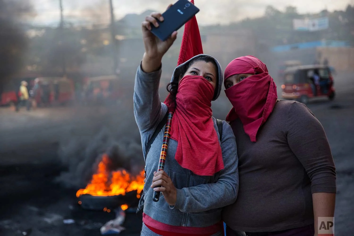 Masked supporters of presidential candidate Salvador Nasralla take a selfie at a burning roadblock set up by demonstrators protesting what they call electoral fraud in Tegucigalpa, Honduras, Friday, Dec. 1, 2017. (AP Photo/Rodrigo Abd)