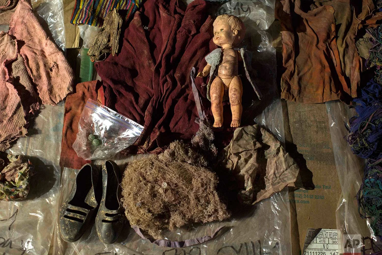 In this Nov. 29, 2017 photo, clothing, earrings and a doll that were found among the remains of over 100 Ixil Mayans exhumed from a mass grave, lay on display for hopeful identification by relatives in Santa Avelina, Guatemala. (AP Photo/Luis Soto)
