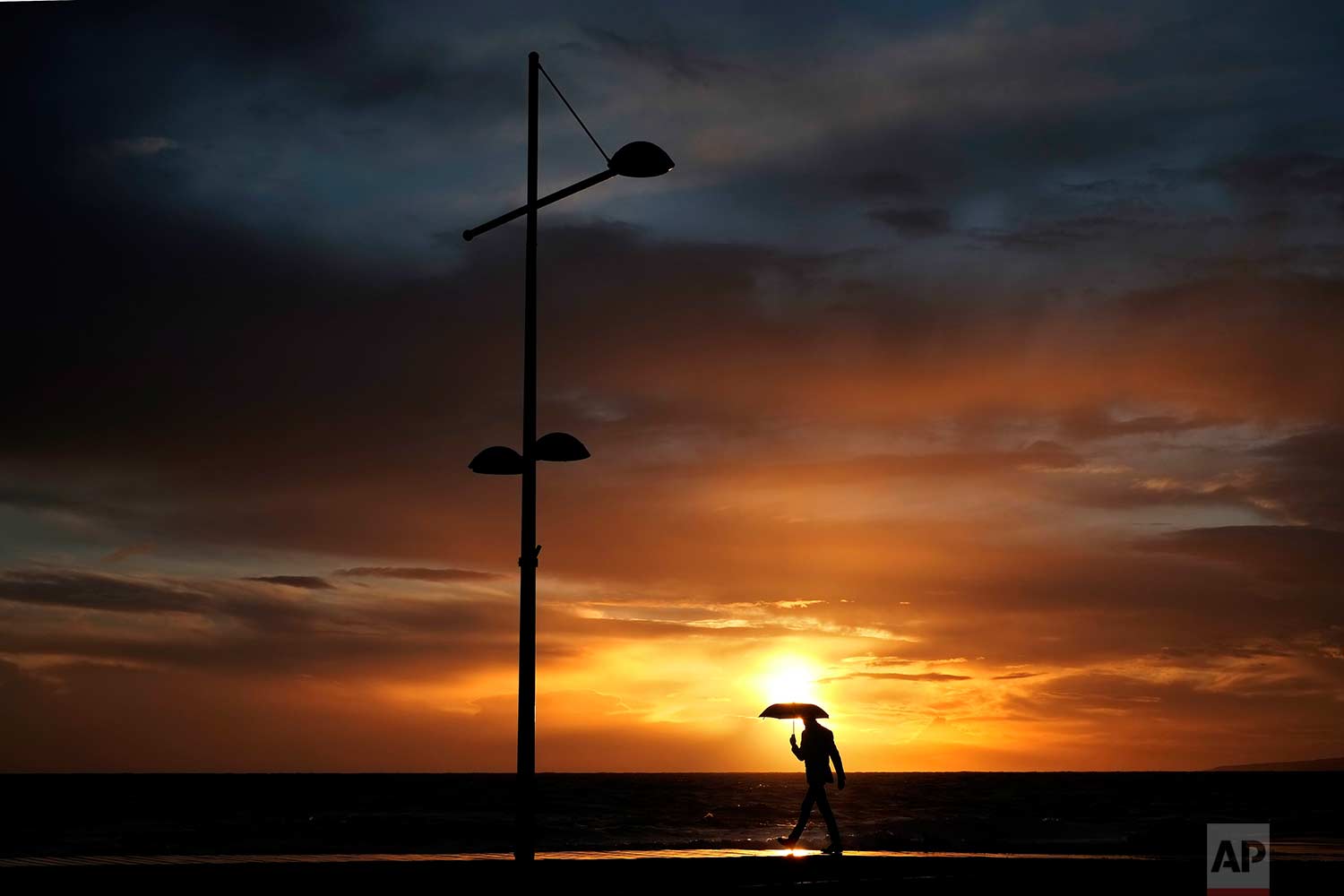  A man with an umbrella walks in the rain as the sun sets at the Ayia Napa resort in the eastern Mediterranean island of Cyprus, Sunday, Dec. 31, 2017. (AP Photo/Petros Karadjias) 