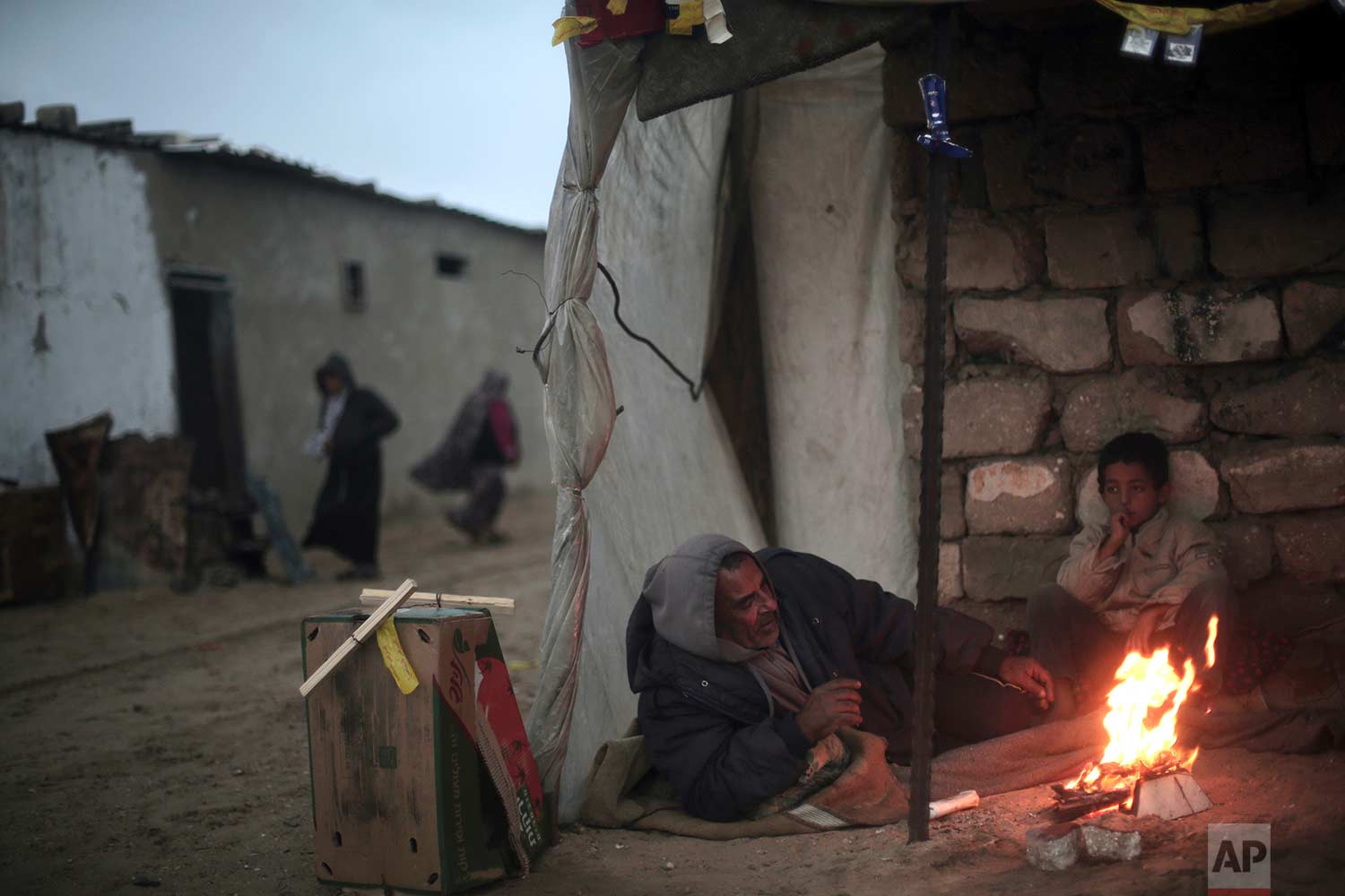  A Palestinian man and his son warm themselves by a fire during cold, rainy weather in a slum on the outskirts of the Khan Younis refugee camp, southern Gaza Strip, Friday, Jan. 5, 2018. (AP Photo/Khalil Hamra) 