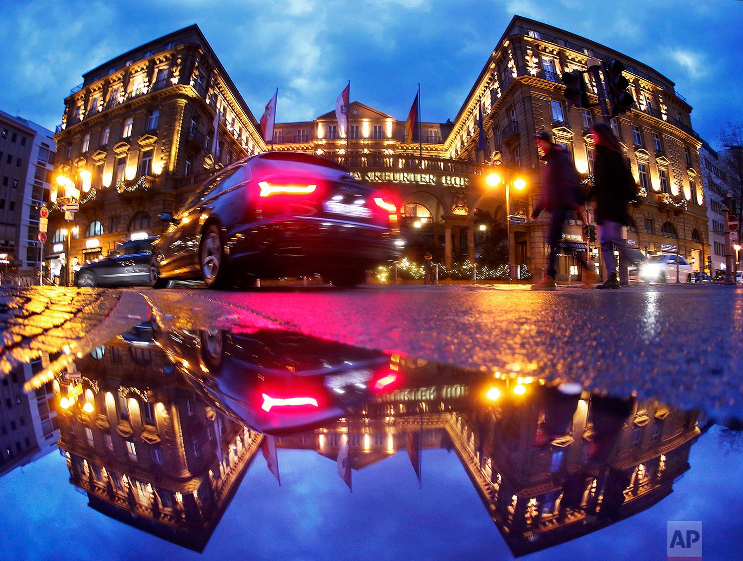  Pedestrians and traffic pass by one of Frankfurt's top hotels, reflected in a puddle, in the city center of Frankfurt, Germany, on Saturday, Dec. 30, 2017. (AP Photo/Michael Probst) 