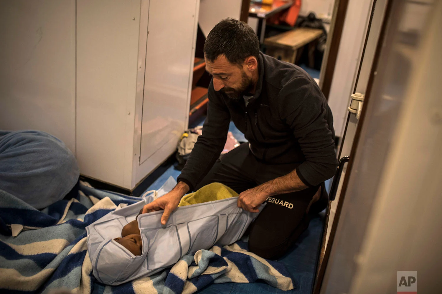In this Thursday, Jan. 18, 2018 photo Guillermo Cañardo, a doctor from the Spanish NGO Proactiva Open Arms, assists an Eritrean child as the organization's rescue vessel heads to Italy with more than 500 refugees and migrants on board. (AP Photo/Santi Palacios) 