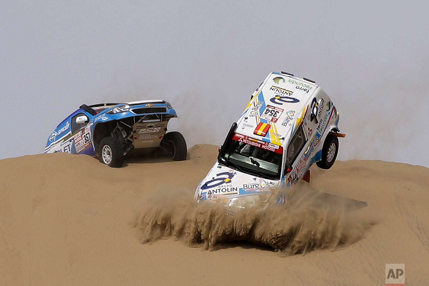  In this Saturday, Jan. 6, 2018 photo, a Mitsubishi car, front, driven by Cristina Gutierrez Herrero and Gabriel Moiset Ferrer, both from Spain, turns over during the first stage of the Dakar Rally between Lima and Pisco, Peru. (AP Photo/Ricardo Maza