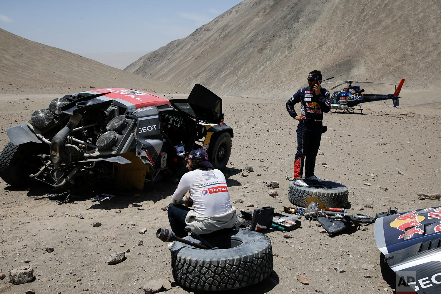  In this Tuesday, Jan. 9, 2018 photo, French driver Cyril Despres, right, tries to contact his team as co-driver David Castera, also French, sits on a tire from their damaged Peugeot during the 4th stage of the Dakar Rally in San Juan de Marcona, Per