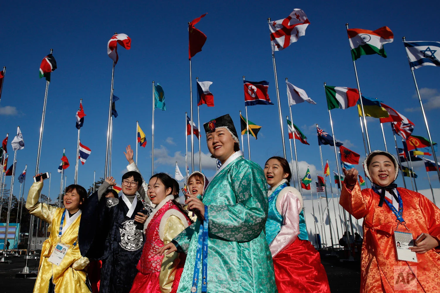 A group of volunteers wearing handbook, Korean traditional dress, greet athletes entering the Olympic Village as flags including North Korea's, fly prior to the 2018 Winter Olympics in Gangneung, South Korea, Thursday, Feb. 1, 2018. (AP Photo/Jae C. Hong)