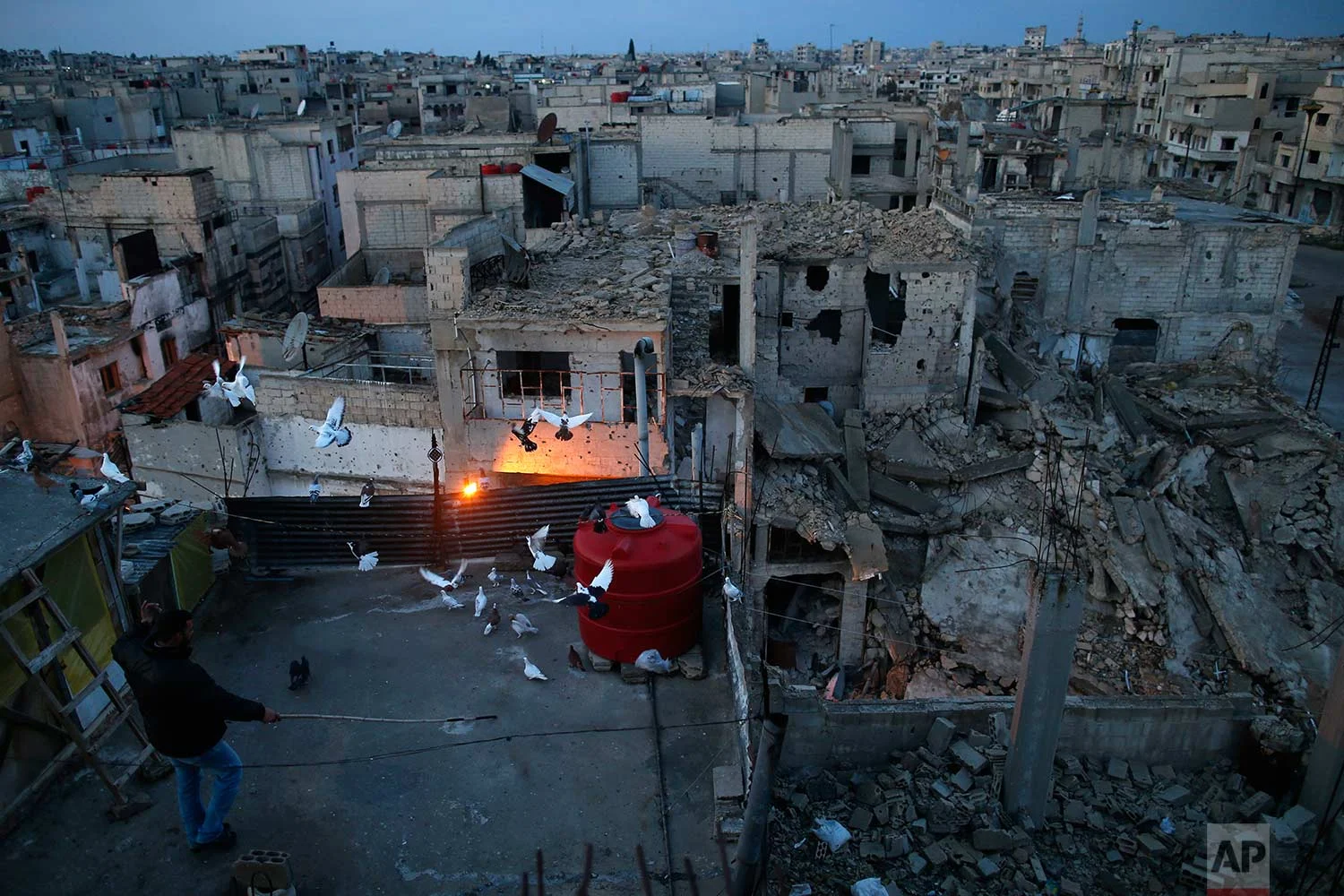 A pigeon keeper watches his birds fly from the roof of his home in the war-damaged Bab Dreib neighborhood of the old city, in Homs, Syria on Jan. 16, 2018. (AP Photo/Hassan Ammar)
