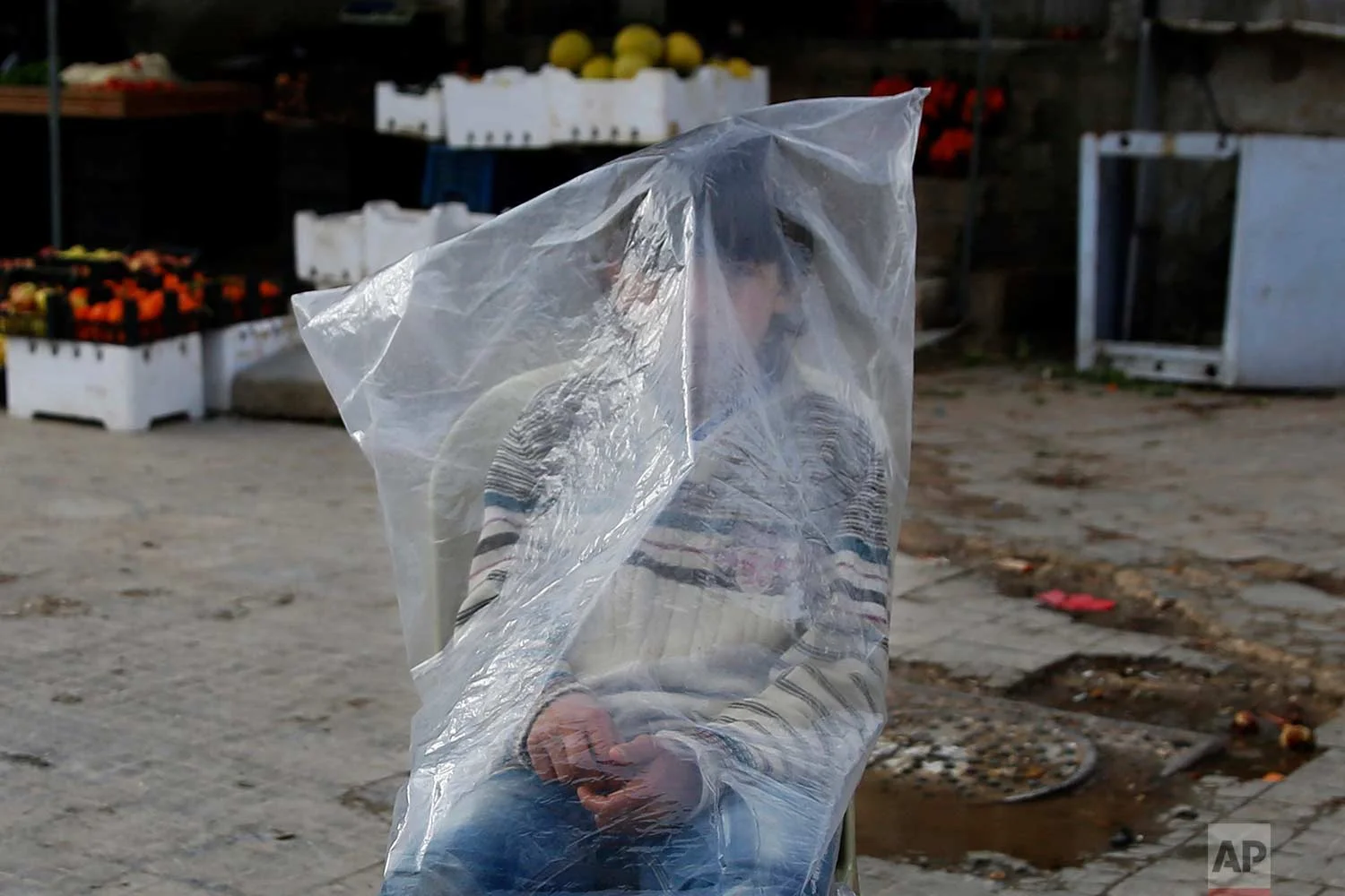 A Syrian boy shields himself from the rain and cold wearing a plastic bag while he sells bread in Aleppo, Syria, Friday, Jan. 19, 2018. (AP Photo/Hassan Ammar)
