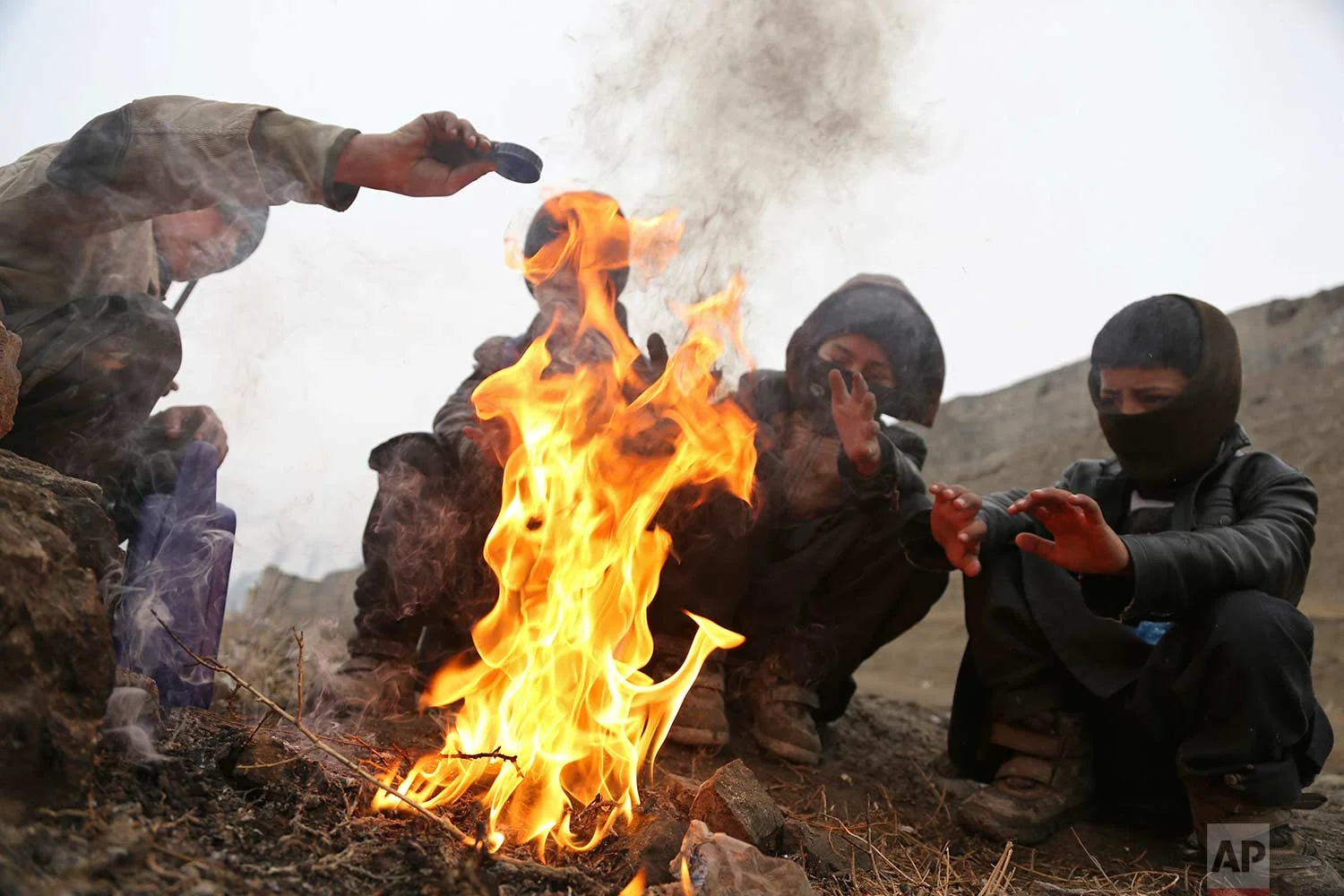 Boys warm themselves near a fire during a rainy day on the outskirts of Kabul, Afghanistan, Wednesday, Jan. 31, 2018. (AP Photo/Rahmat Gul)