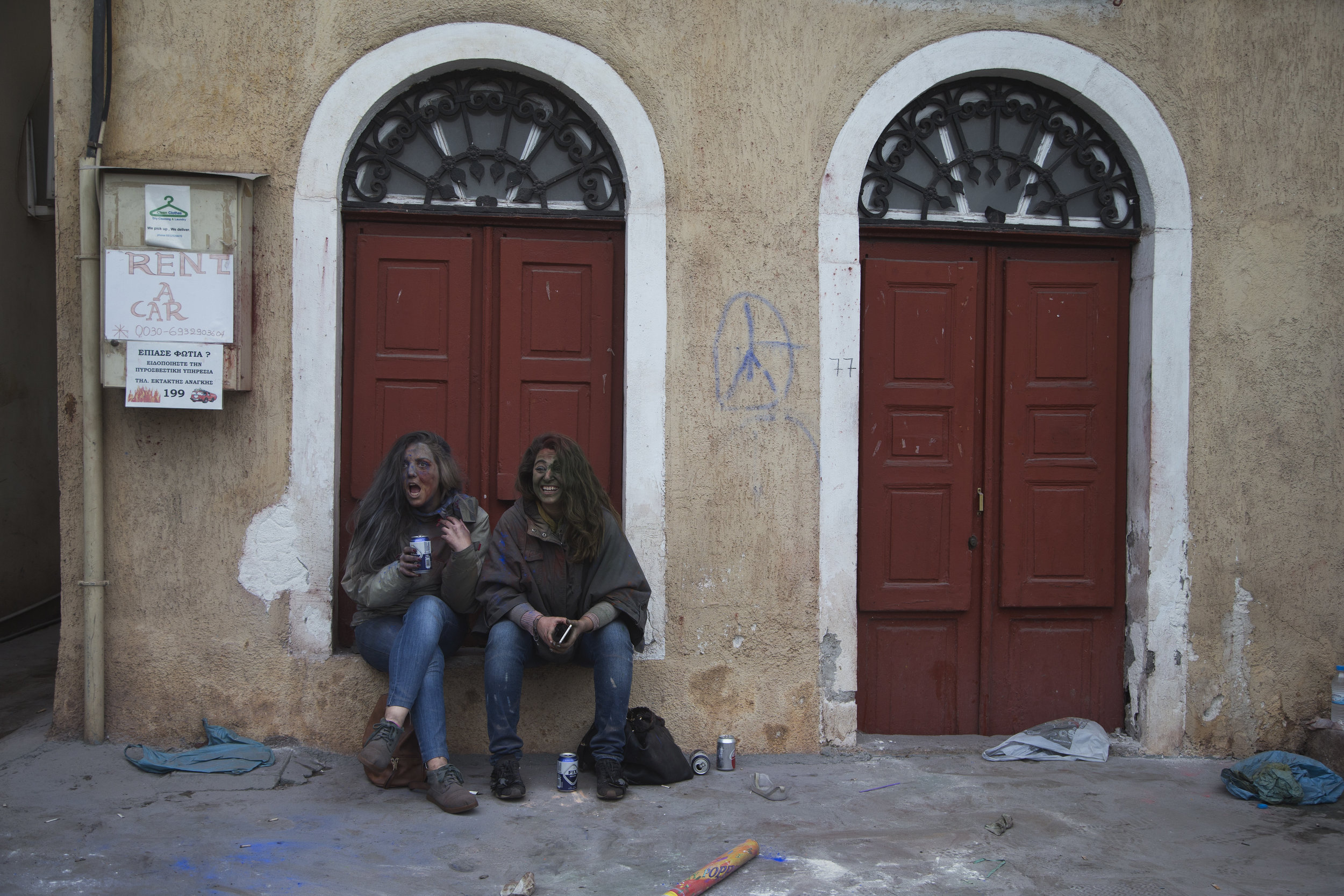  In this Monday, Feb. 19, 2018 photo, twin sisters sit outside a house as they watch revelers taking part in the flour war, a unique colorful flour fight marking the end of the carnival season in the port town of Galaxidi, some 200 kilometers (120 mi