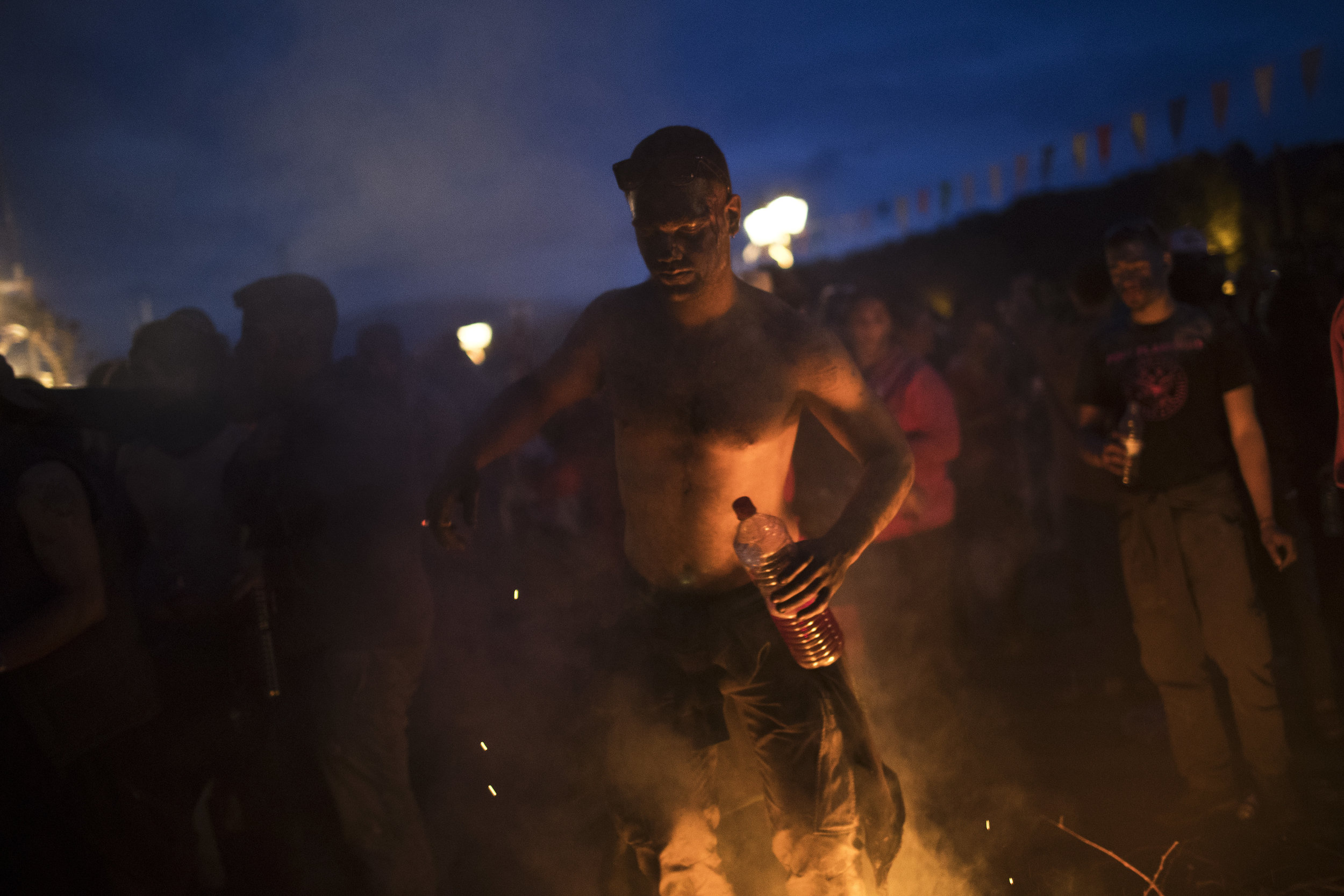  In this Monday, Feb. 19, 2018 photo, a reveler with a bottle of wine dances near a fire during the flour war, a unique colorful flour fight marking the end of the carnival season in the port town of Galaxidi, some 200 kilometers (120 miles) west of 