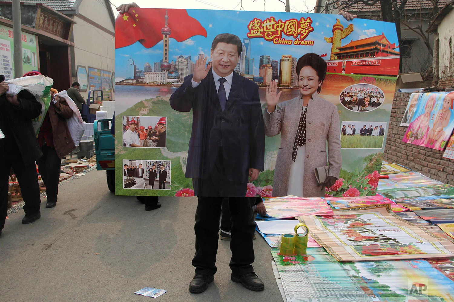  In this Jan. 28, 2016, photo, a vendor holds up a poster of Chinese President Xi Jinping and First Lady Peng Liyuan in a rural market during Chinese New Year season when locals traditionally paste new posters on the walls of their home in Binzhou in