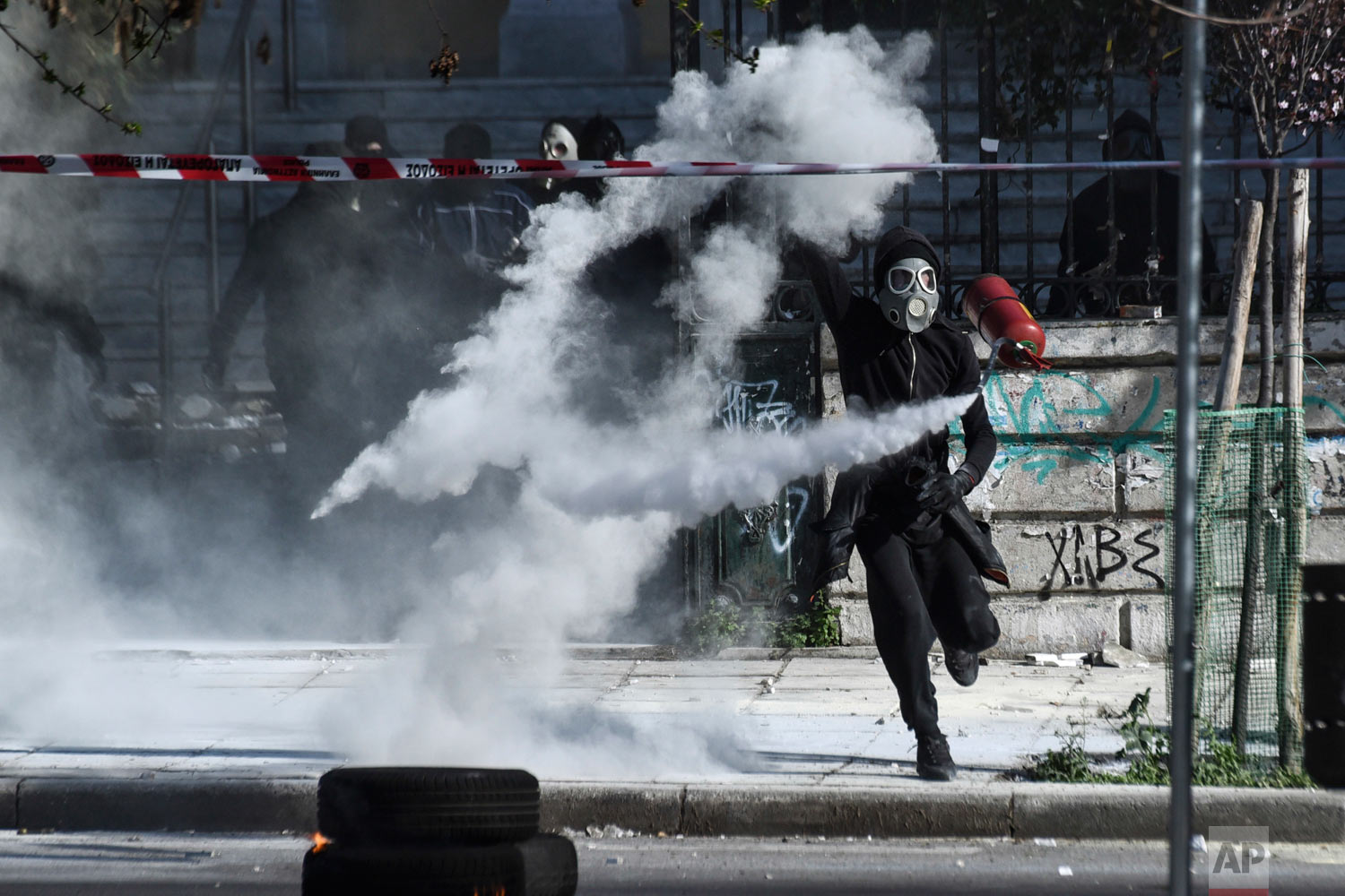  A masked protester confronts riot police outside the University of Thessaloniki campus in Thessaloniki, Greece on Saturday, March 10, 2018. Anarchists have clashed with riot police in Greece after some 2,000 demonstrators from across the Balkans mar