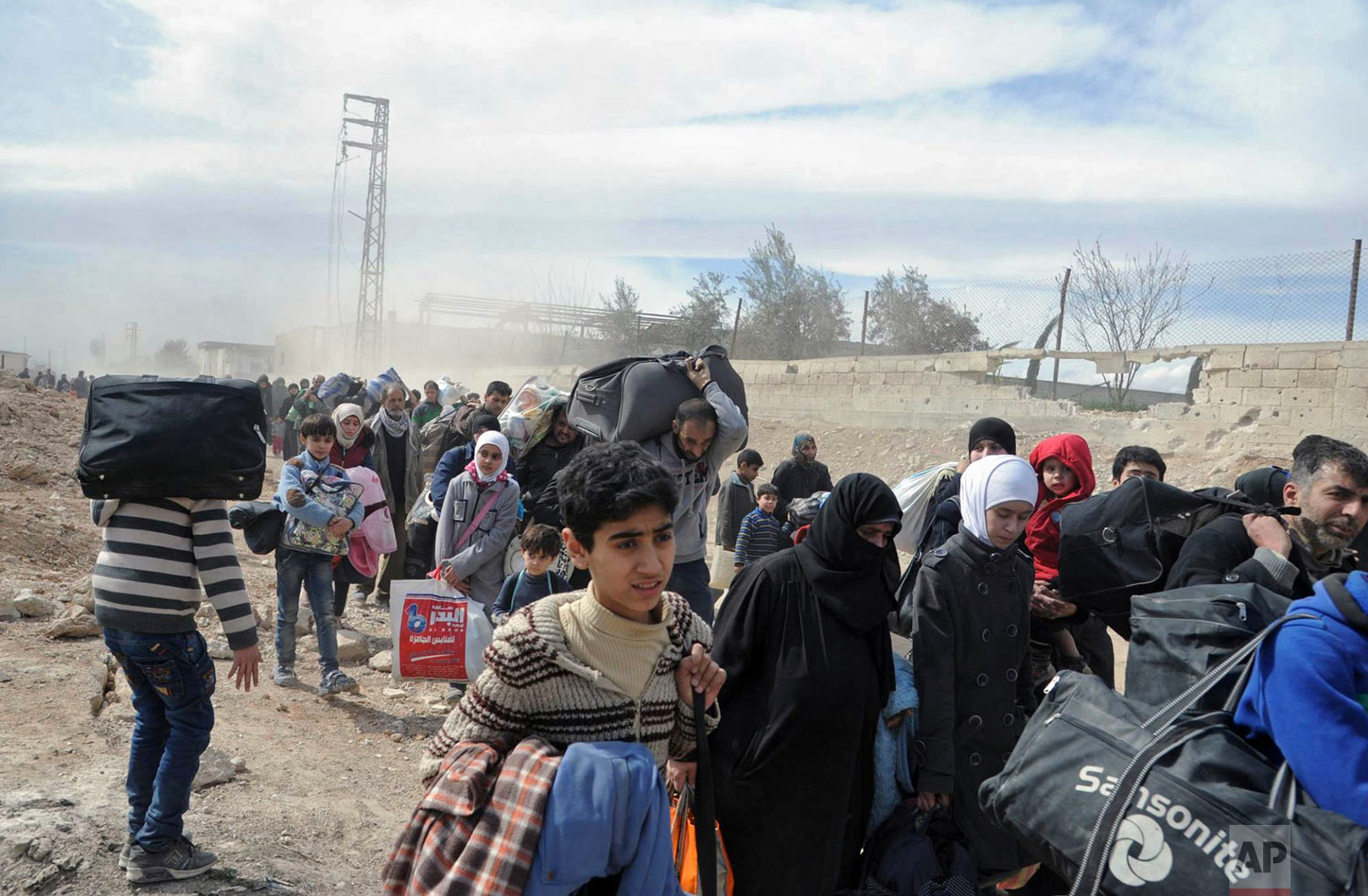 In this photo released by the Syrian official news agency SANA, civilians carry their belongings as they flee from fighting between Syrian government forces and rebels in Hamouria in eastern Ghouta, a suburb of Damascus, Syria, on Thursday, March. 15, 2018. Thousands streamed out of Syria's besieged, opposition-held enclave of eastern Ghouta on Thursday, crossing on foot and in pick-up trucks and tractors to government-held territory near the capital, Damascus, according to footage on state-run Syrian television. (SANA via AP)