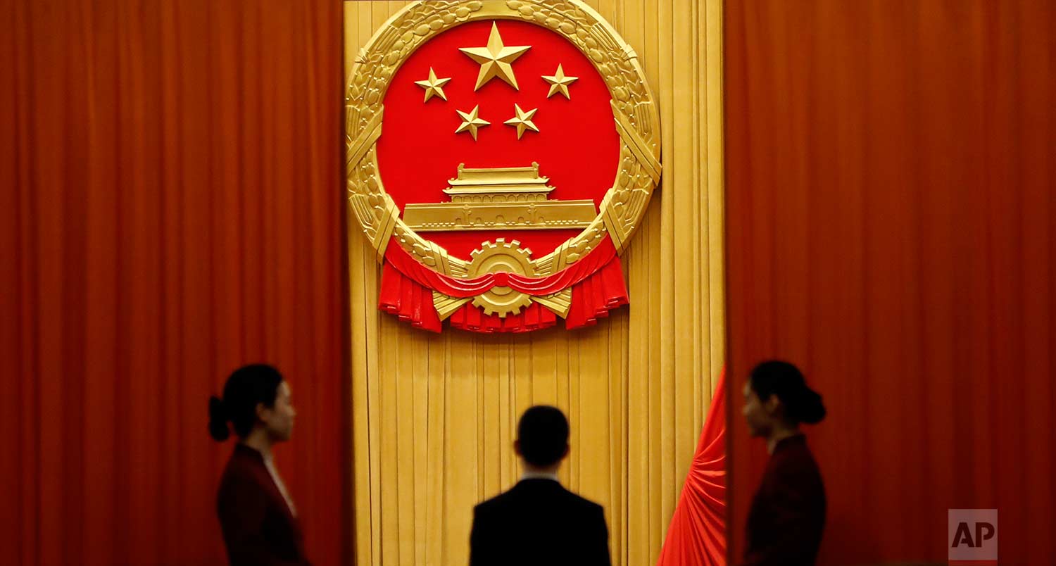  In this Tuesday, March 13, 2018 photo, attendants stand behind curtains below the red and yellow Chinese national emblem before the start of a plenary session of China's National People's Congress (NPC) at the Great Hall of People in Beijing. (AP Ph