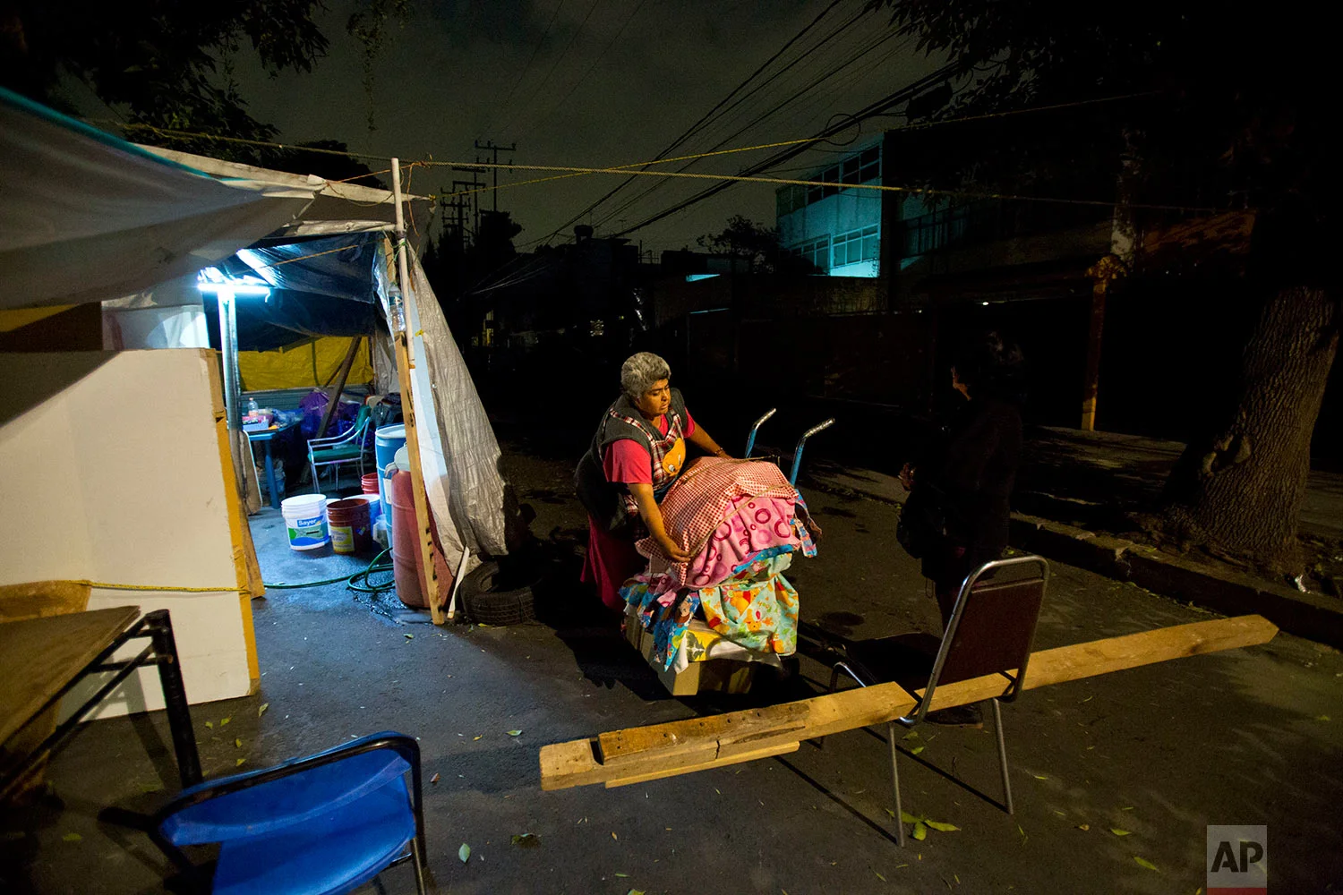 Vendor Maria Patricia Rodriguez Gonzalez packs up her wares to bring them in for the night, at the tent camp where she has been living with her family for the last six months, outside her earthquake-damaged residence at Independencia 18 in Mexico City, March 14, 2018. (AP Photo/Rebecca Blackwell)