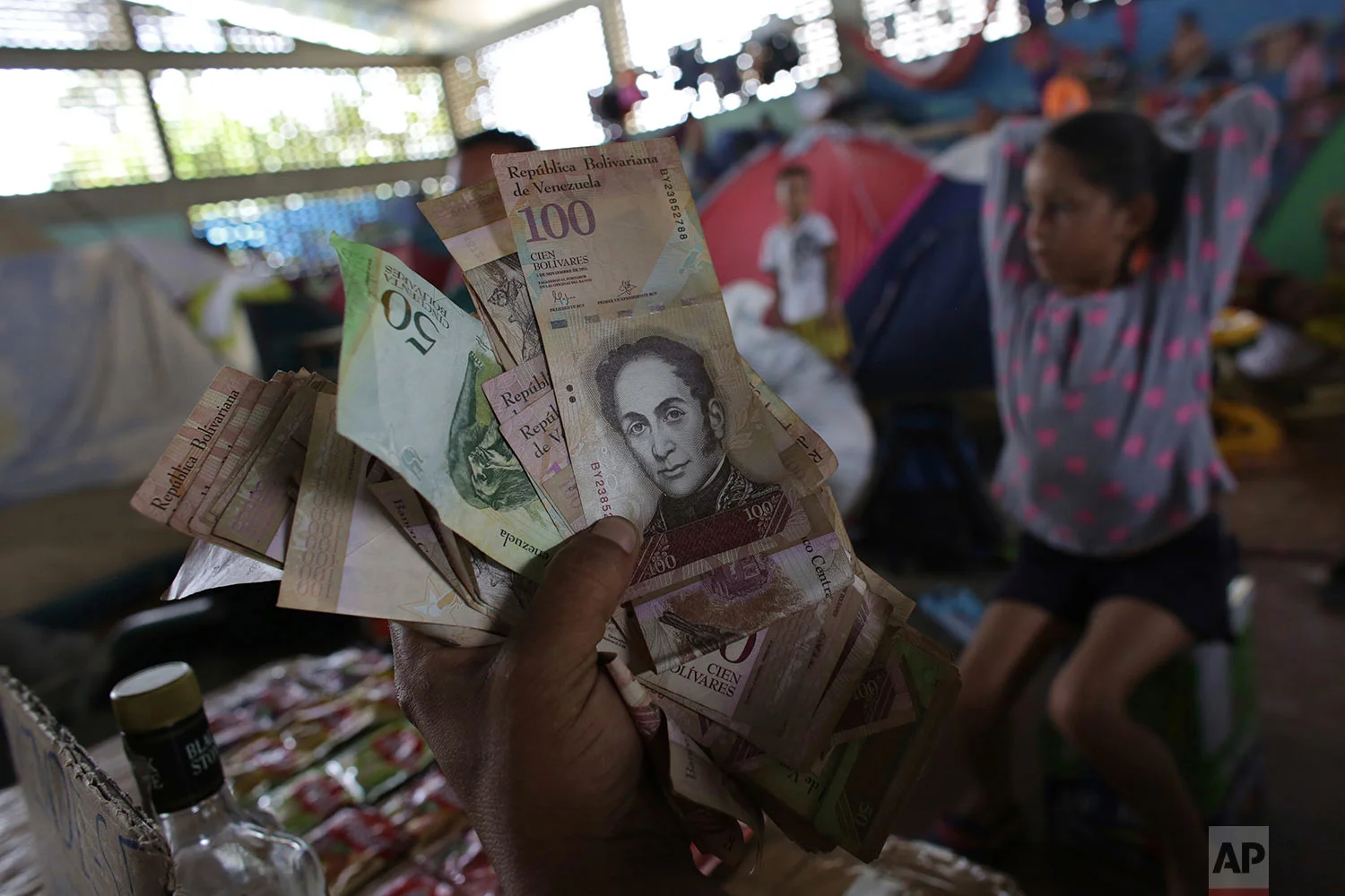Venezuelan migrant Charlie Ivan Delgado shows his country's currency as he talks about the economic crisis at a migrant shelter that offers three meals a day where he brought his family of five, inside the Tancredo Neves Gymnasium in Boa Vista, Roraima state, Brazil, March 8, 2018. (AP Photo/Eraldo Peres)