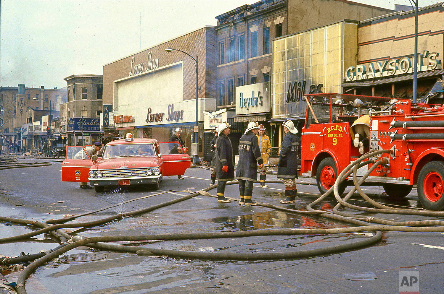  14th Street near Irving Street, 1968. Firemen gathered at a fire engine on 14th Street near Irving Street following rioting after the assassination of Dr. Martin Luther King, Jr., Saturday, April 6, 1968. Firehouses cover the ground. Burned storefro