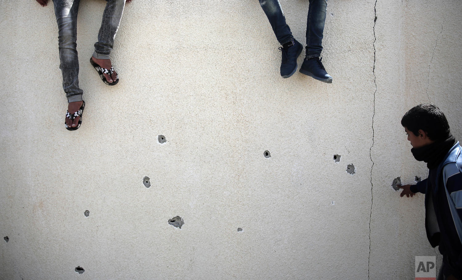 Palestinians check bullet holes in a wall following an exchange of gunfire between Palestinian Hamas security forces and suspects wanted for a bombing that targeted the visiting Palestinian premier's convoy last week in Gaza, in the town of Nuseirat, central Gaza Strip, Thursday, March 22, 2018. (AP Photo/ Khalil Hamra)
