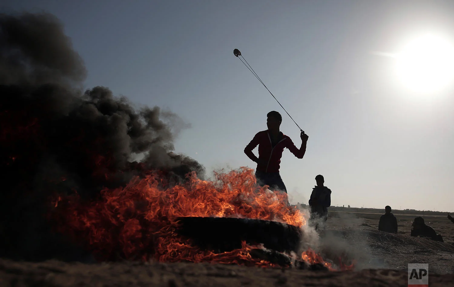 A Palestinian protester hurls stones toward Israeli soldiers during a protest near the Gaza Strip border with Israel, in eastern Gaza City, Saturday, March 31, 2018. (AP Photo/ Khalil Hamra)