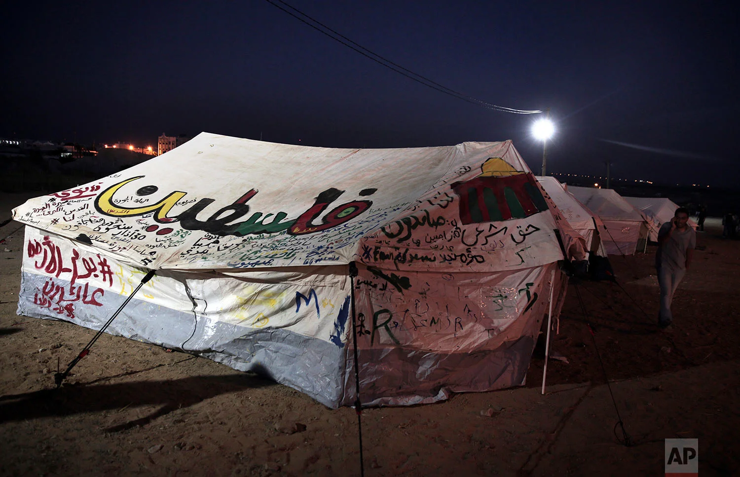 Palestinians walk between their family tents which set up in front the Gaza Strip border with Israel, east of Beit Lahiya, Gaza Strip, Saturday, March 31, 2018. (AP Photo/Adel Hana)