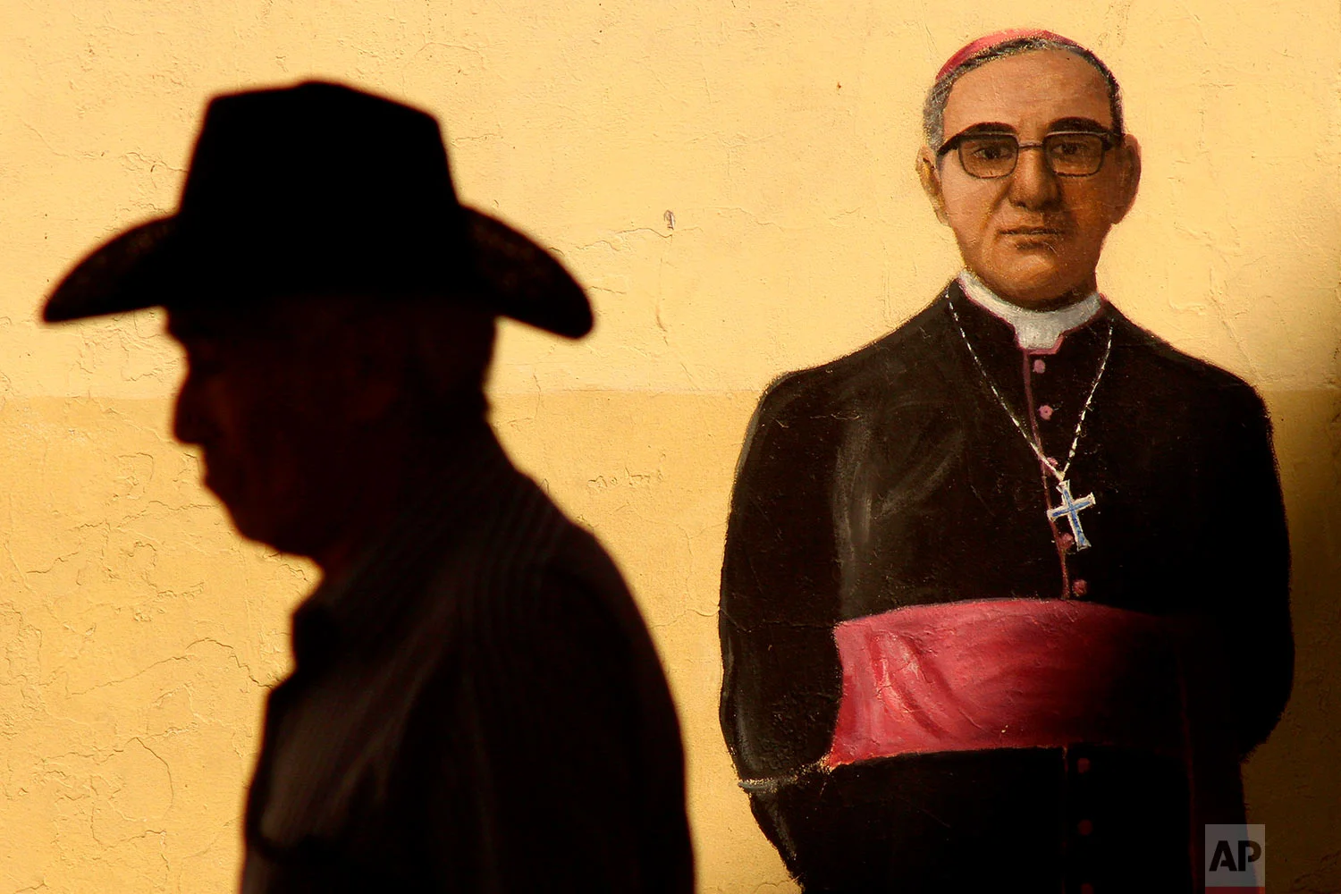 A man walks past a mural of late Archbishop Oscar Arnulfo Romero outside the Metropolitan Cathedral where Mass was offered to mark the 38th anniversary of the archbishop's death, in San Salvador, El Salvador, March 24, 2018. Pope Francis declared earlier this month that the churchman who became a hero for standing up for the poor and oppressed should be canonized along with the reformer Pope Paul VI. (AP Photo/Salvador Melendez)