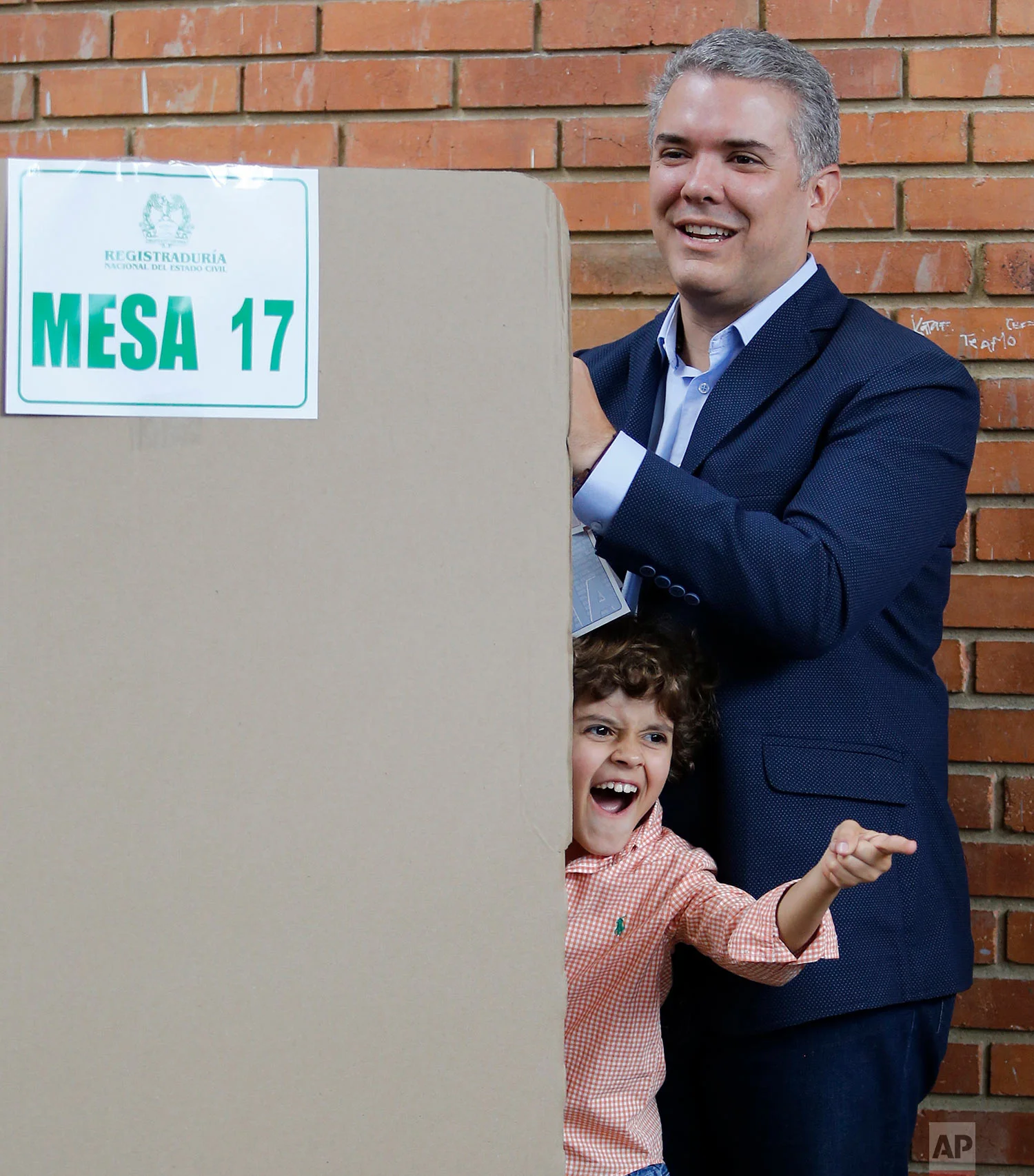 Ivan Duque, presidential candidate with the Democratic Center party, marks his vote during legislative elections as his son makes faces at his family and members of the press in Bogota, Colombia, March 11, 2018. Colombia will hold presidential elections in May. (AP Photo/Fernando Vergara)
