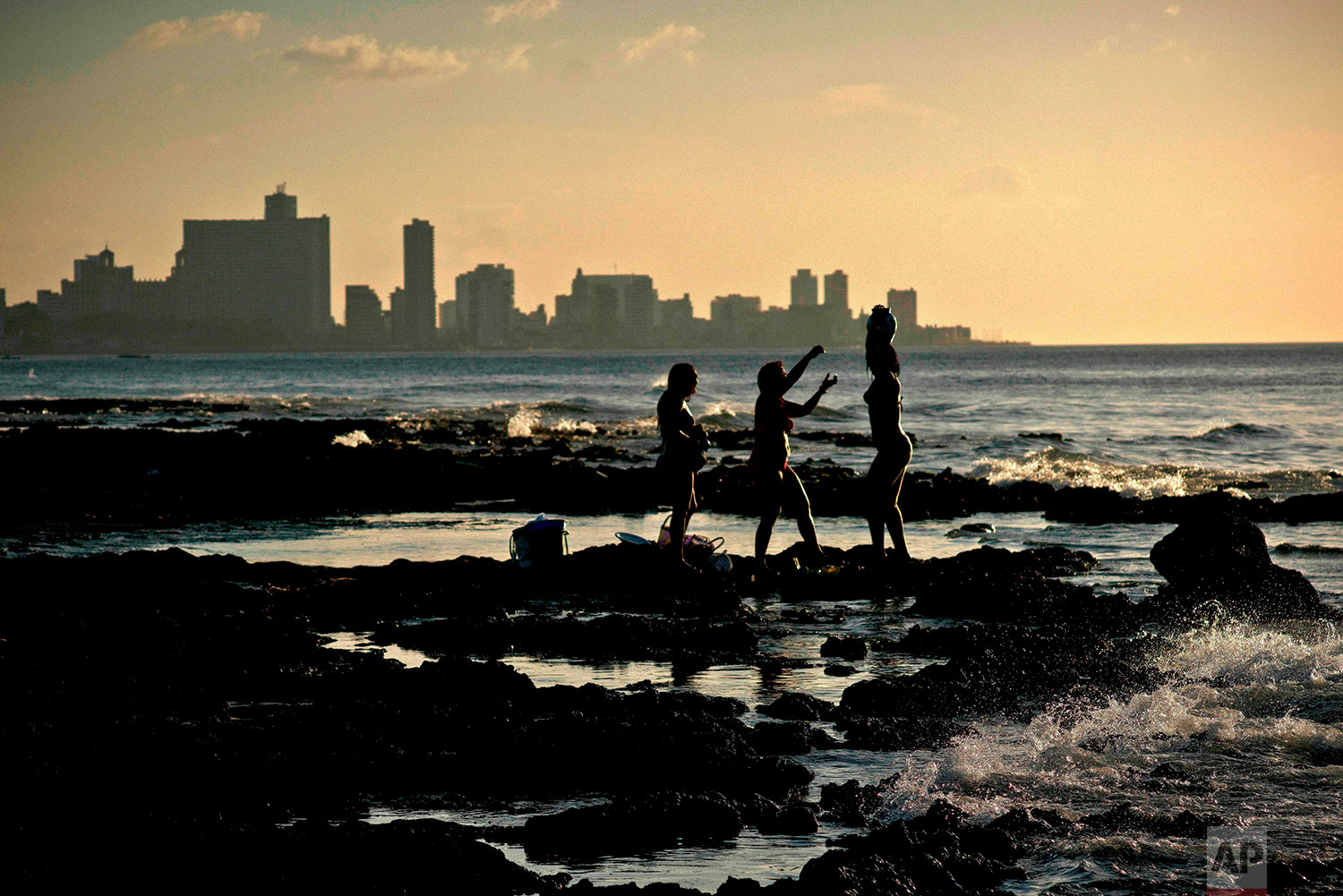 In this April 14, 2018 photo, Santera Mailyn Lopez, center, performs a ritual with Mili Garcia Perez, right, and Zulay De Las Mercedes, on Chivo beach in Havana, Cuba. Mili and Zulay, who work at a restaurant, came to evoke the presence of “Olokun,” a saint who according to Santeria lives in the sea and brings one health, prosperity and stability. (AP Photo/Ramon Espinosa)