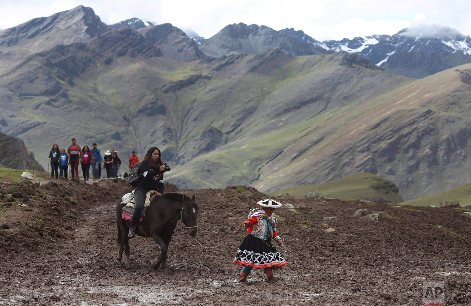  In this March 2, 2018 photo, a group of tourists ride horses led by an Andean guide to Rainbow Mountain, a ridge of multicolored sediments laid down millions of years ago and pushed up as tectonic plates clashed, in Pitumarca, Peru. (AP Photo/Martin