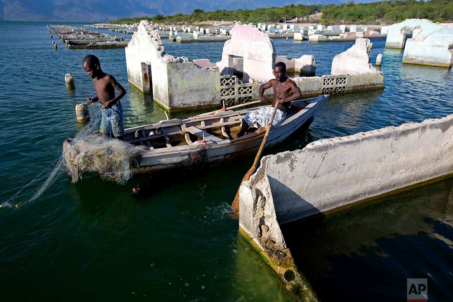  In this April 20, 2018 photo, fisherman Miguel Louis checks on his nets with his 12-year-old son Dabens Louis, placed amid old, abandoned flooded homes on Lake Azuei in Fond Parisien, Haiti. A fish farming company growing tilapia set up their operat