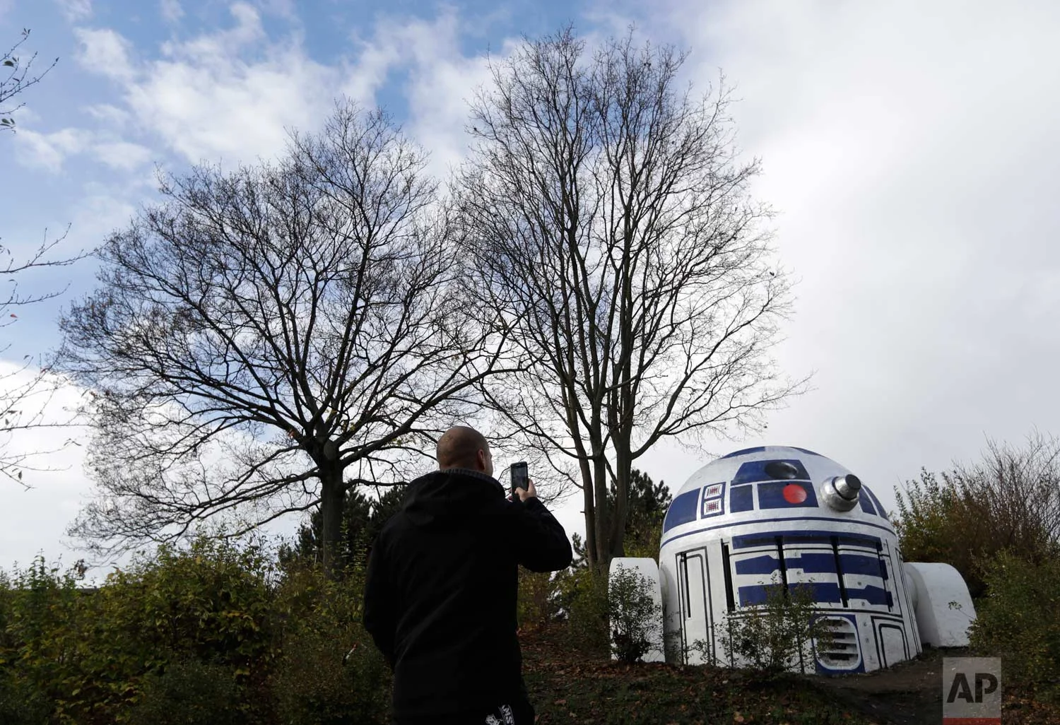 A man takes a photo of an air ventilation turned by an unknown street artist into Star Wars' R2-D2 in a park in Prague, Czech Republic, Saturday, Oct. 28, 2017. According to Prague 2 district mayor, Jana Cernochova, the robot is there to stay. "We do not support illegal graffiti, of course, but we like the decor on this unsightly shaft," she said to local media. (AP Photo/Petr David Josek)