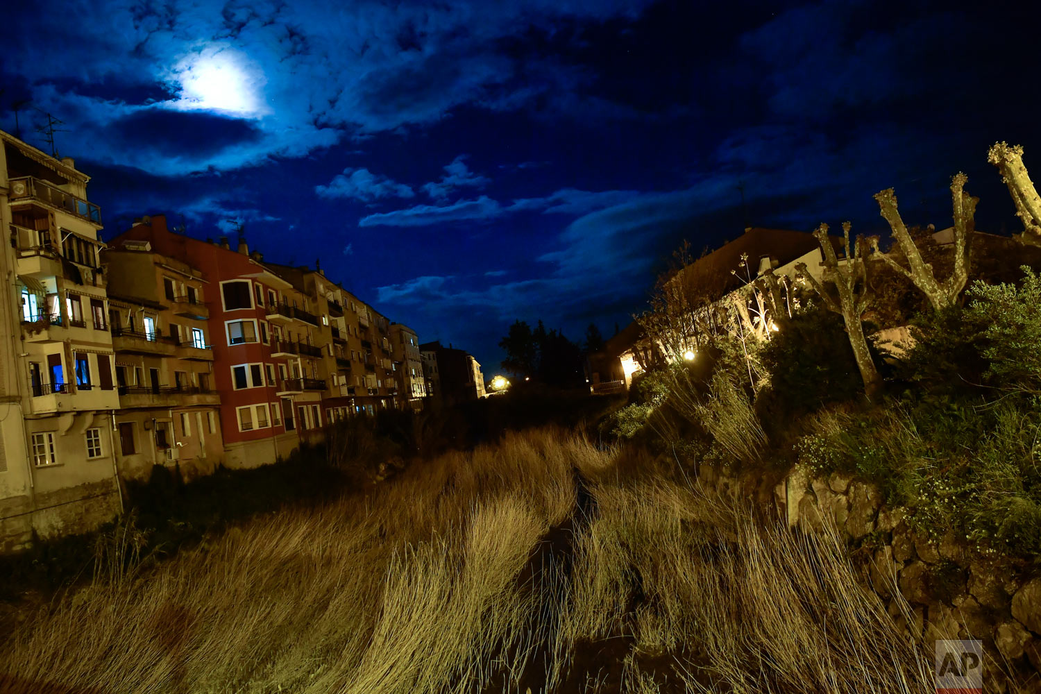 A moon light illuminates the sky through the clouds over a large line of grass between some home houses in the small village of Tafalla, northern Spain, Tuesday, May 1, 2018. (AP Photo/Alvaro Barrientos)